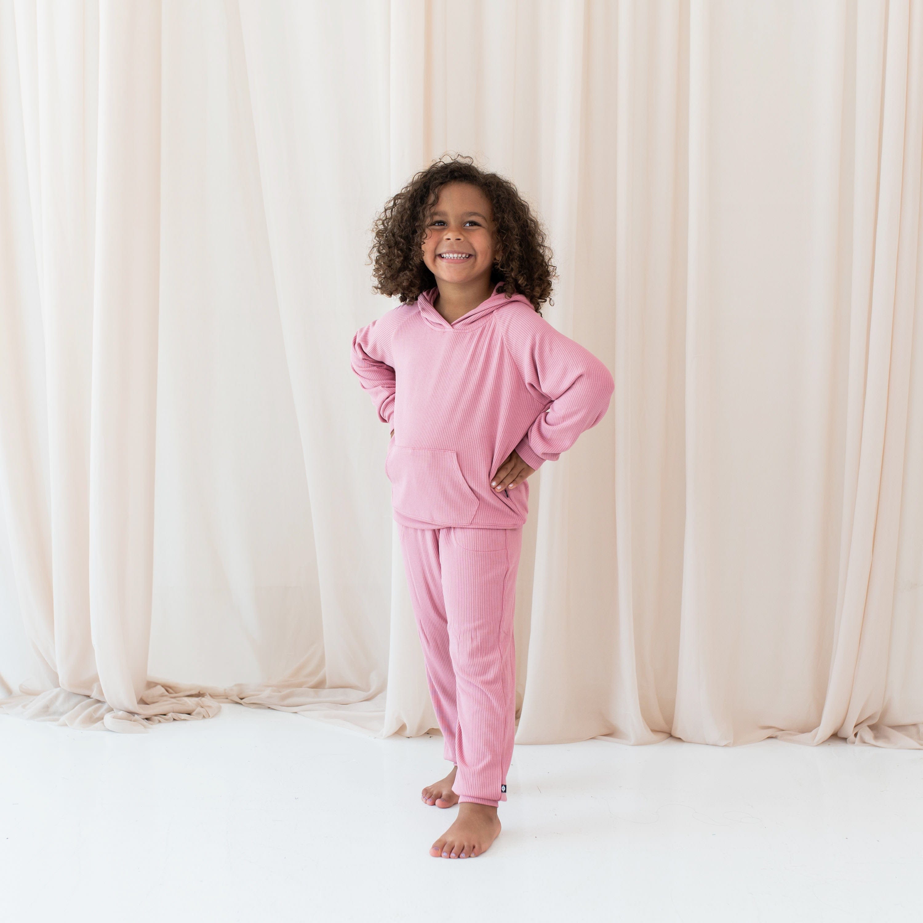 Girl wearing Kyte Baby Ribbed Jogger Hoodie and Pant set in Apple Blossom pink