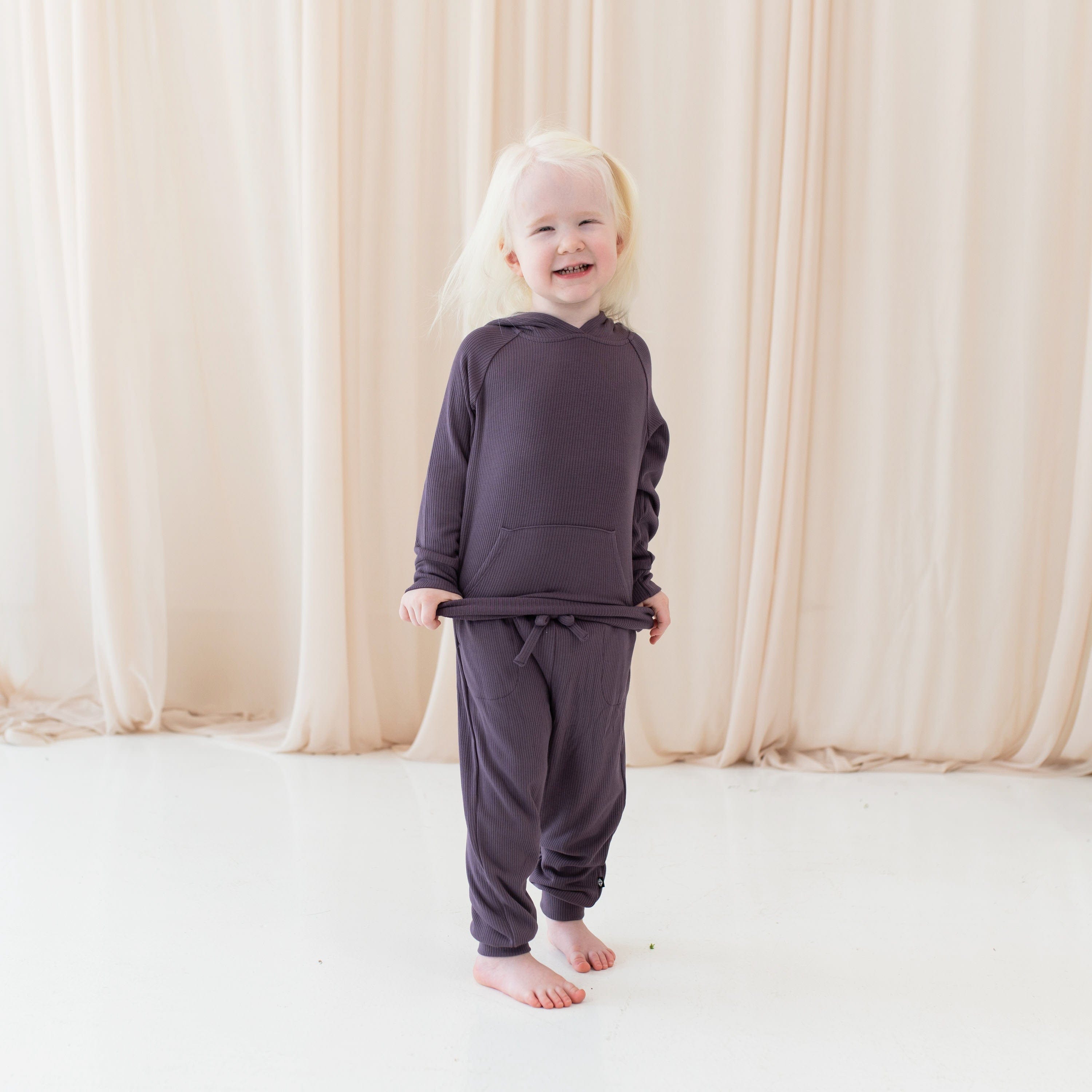 Girl wearing Kyte Baby Ribbed Hoodie and Jogger Pant set in Currant purple