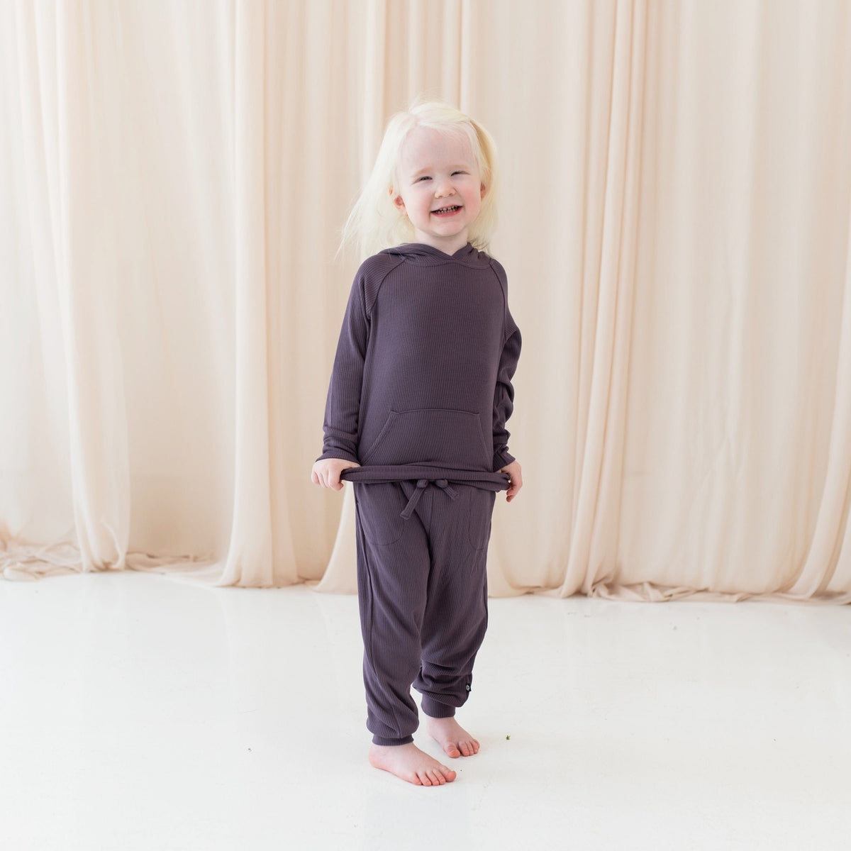 Girl wearing Kyte Baby Ribbed Hoodie and Jogger Pant set in Currant purple
