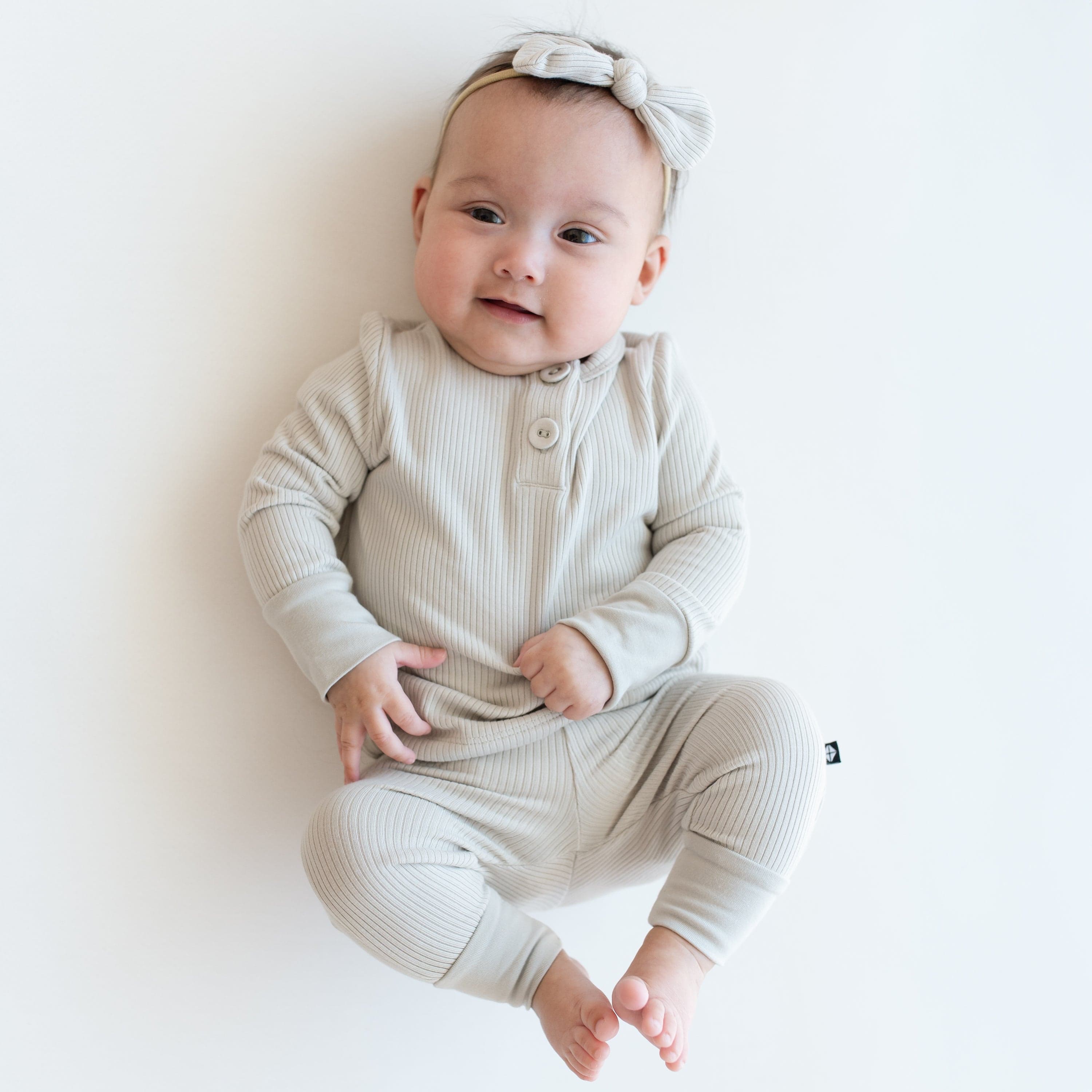 Child wearing Kyte Baby Bamboo Ribbed Infant Henley Set with matching Nylon Bow in Oat