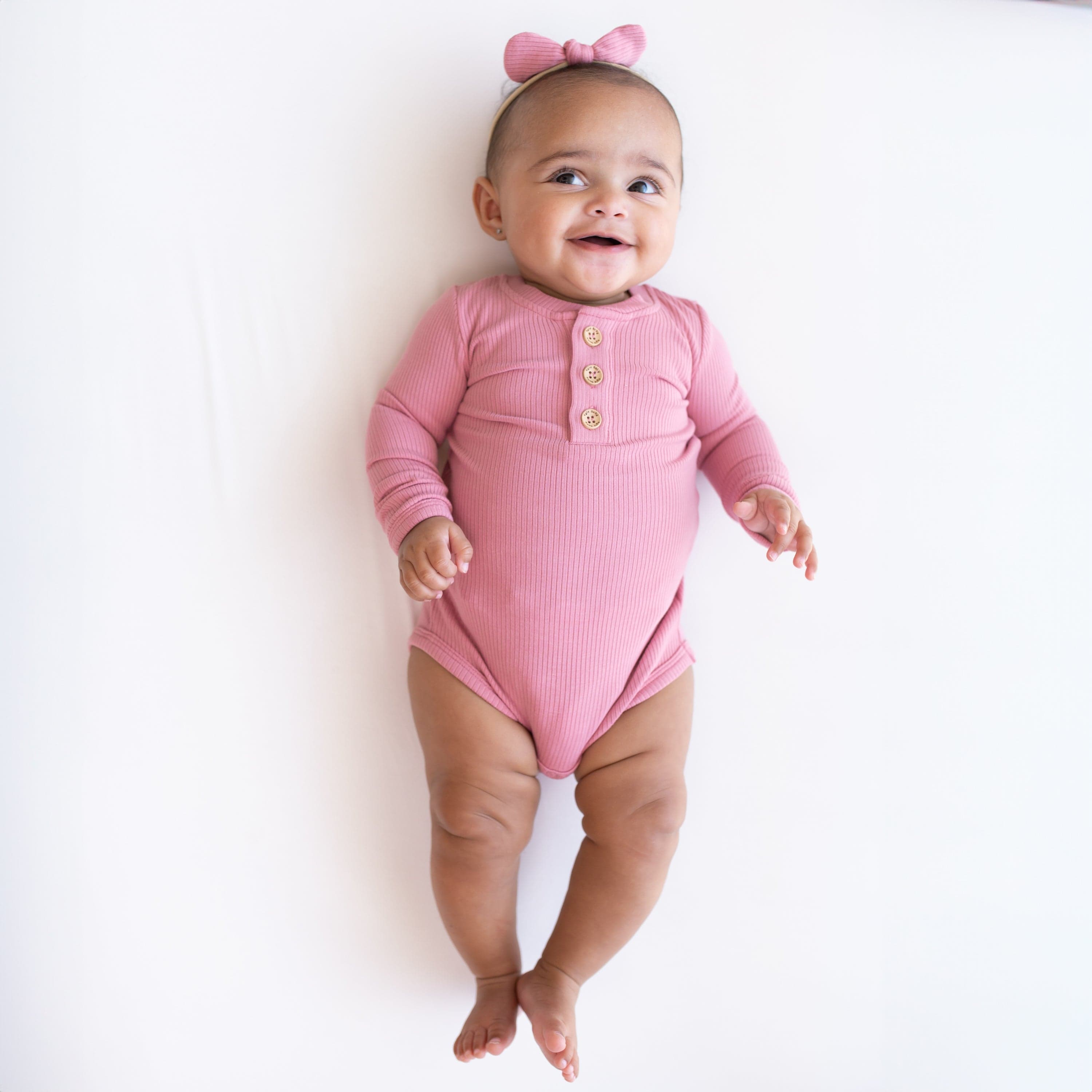 Infant wearing Kyte Baby Ribbed Long Sleeve Henley Bodysuit in Apple Blossom