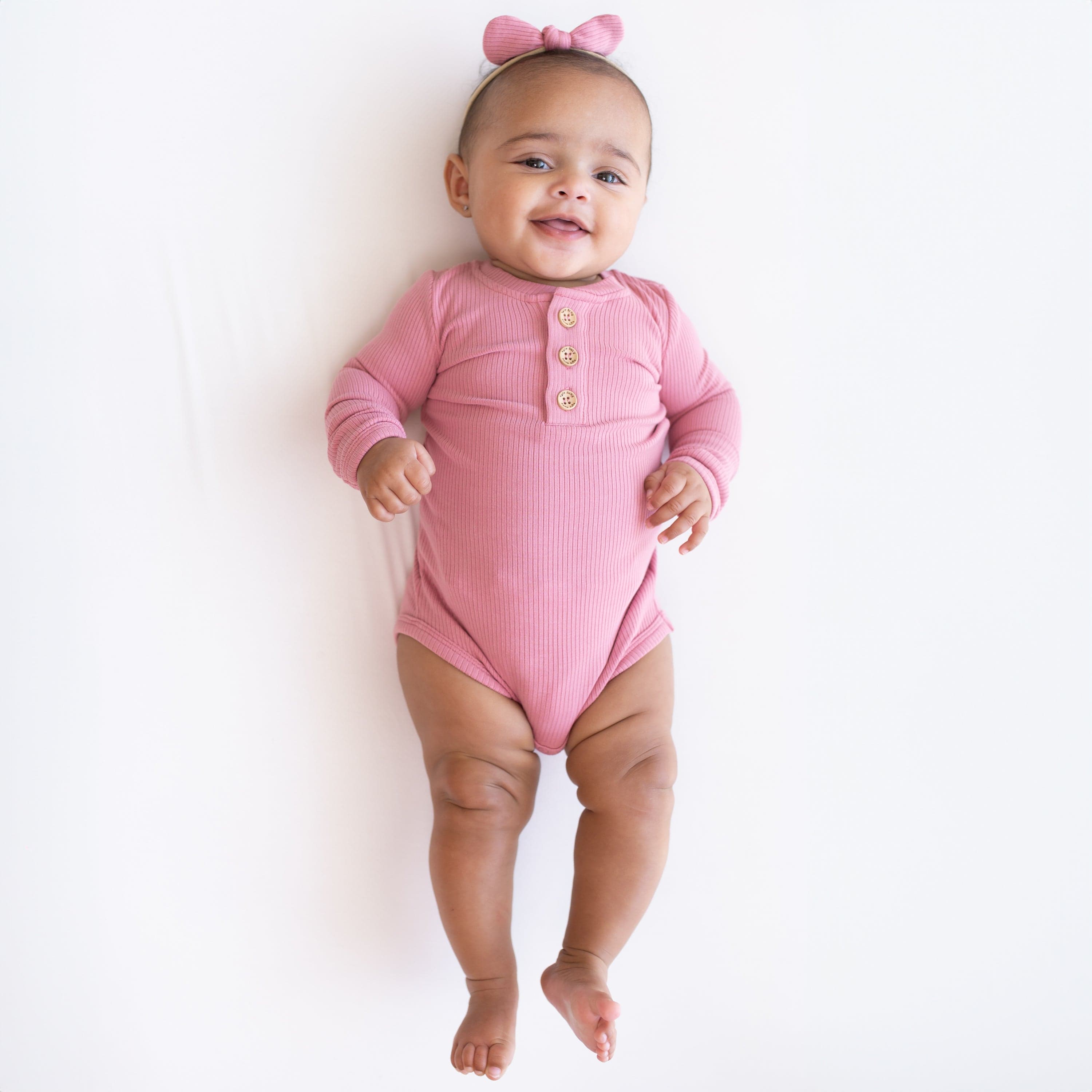Infant wearing Kyte Baby Ribbed Long Sleeve Henley Bodysuit with snap closure in Apple Blossom