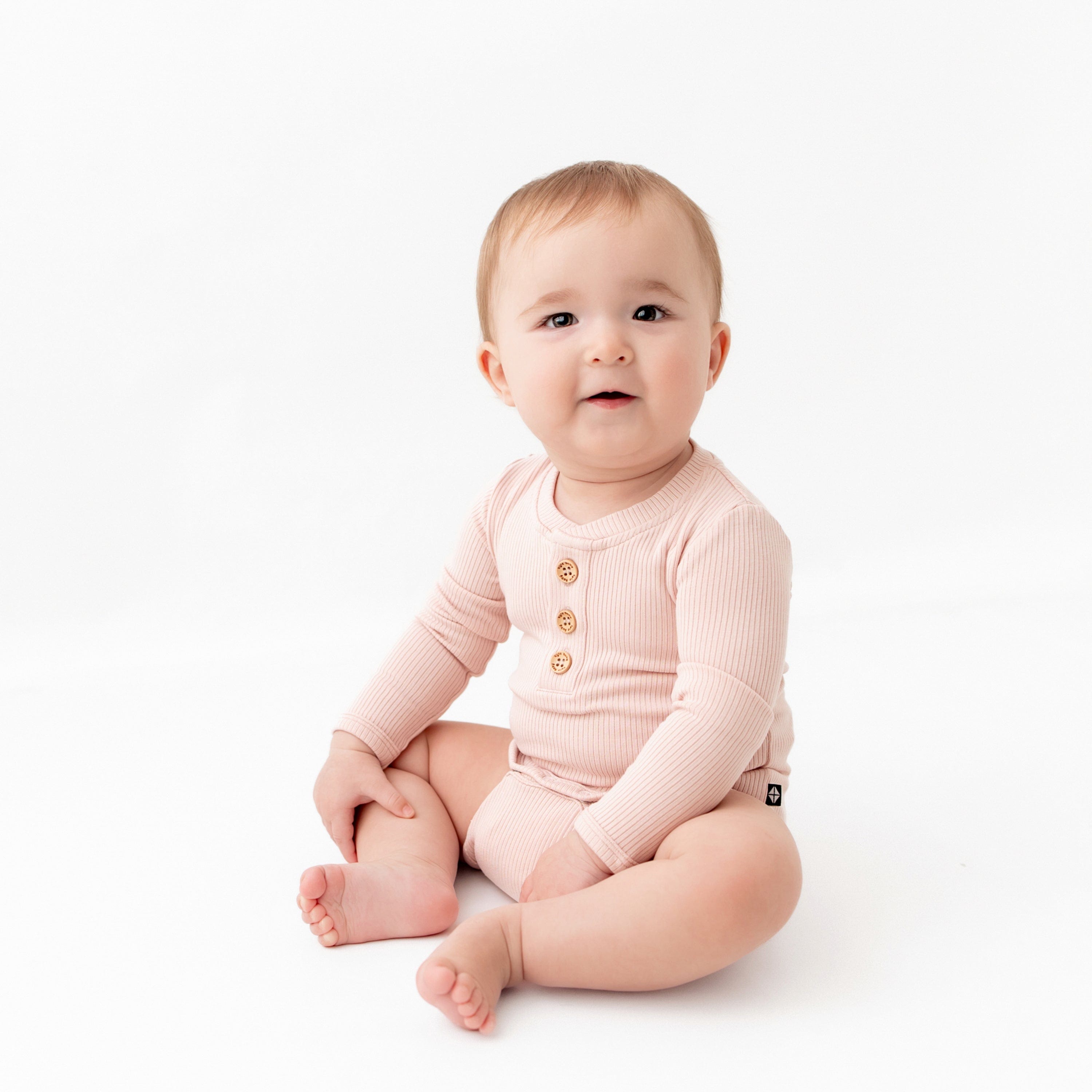Infant wearing Kyte Baby Ribbed Long Sleeve Henley Bodysuit with snap closure in Blush