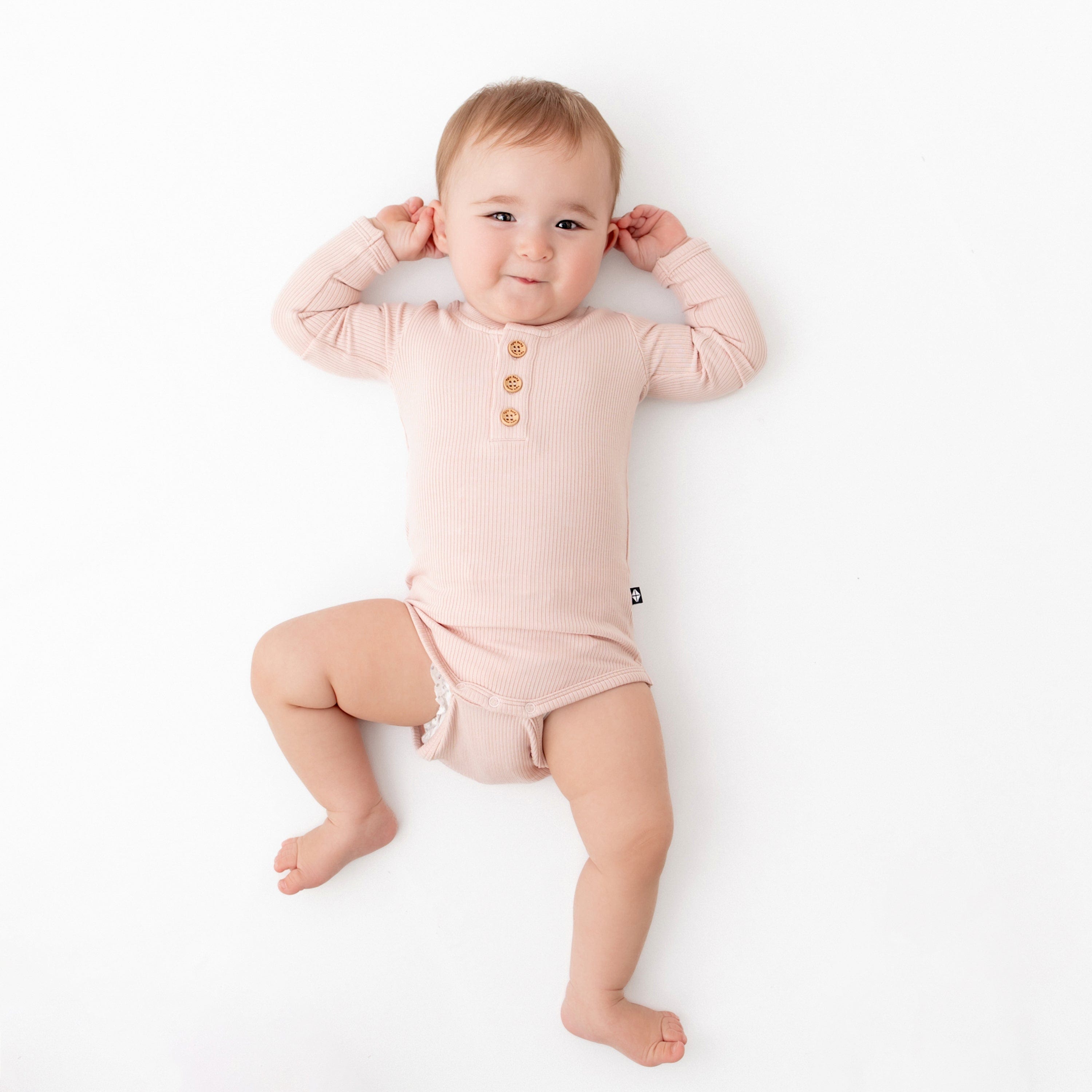 Infant wearing Kyte Baby Ribbed Long Sleeve Henley Bodysuit in Blush