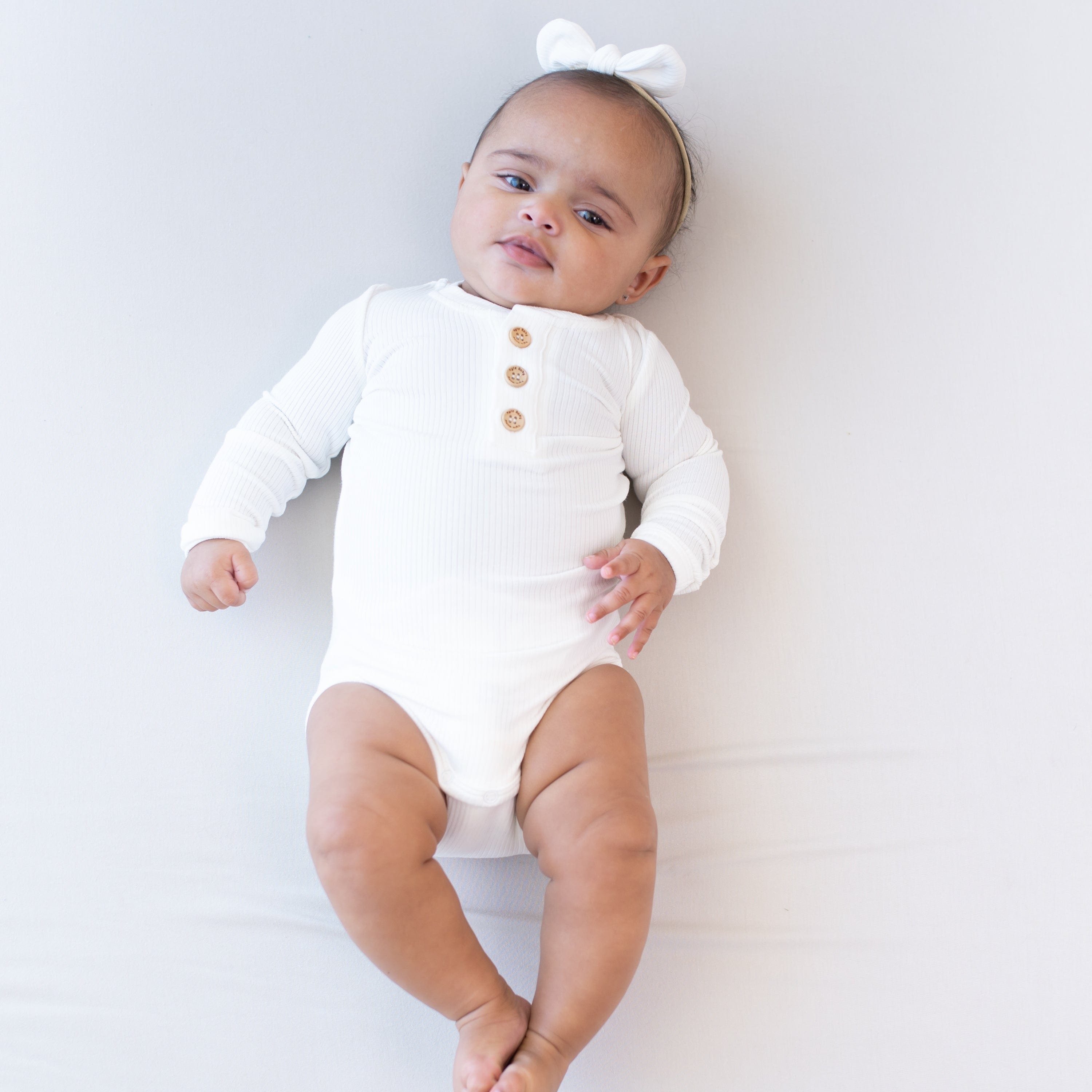 Infant wearing Kyte Baby Ribbed Long Sleeve Henley Bodysuit with snap closure in Cloud