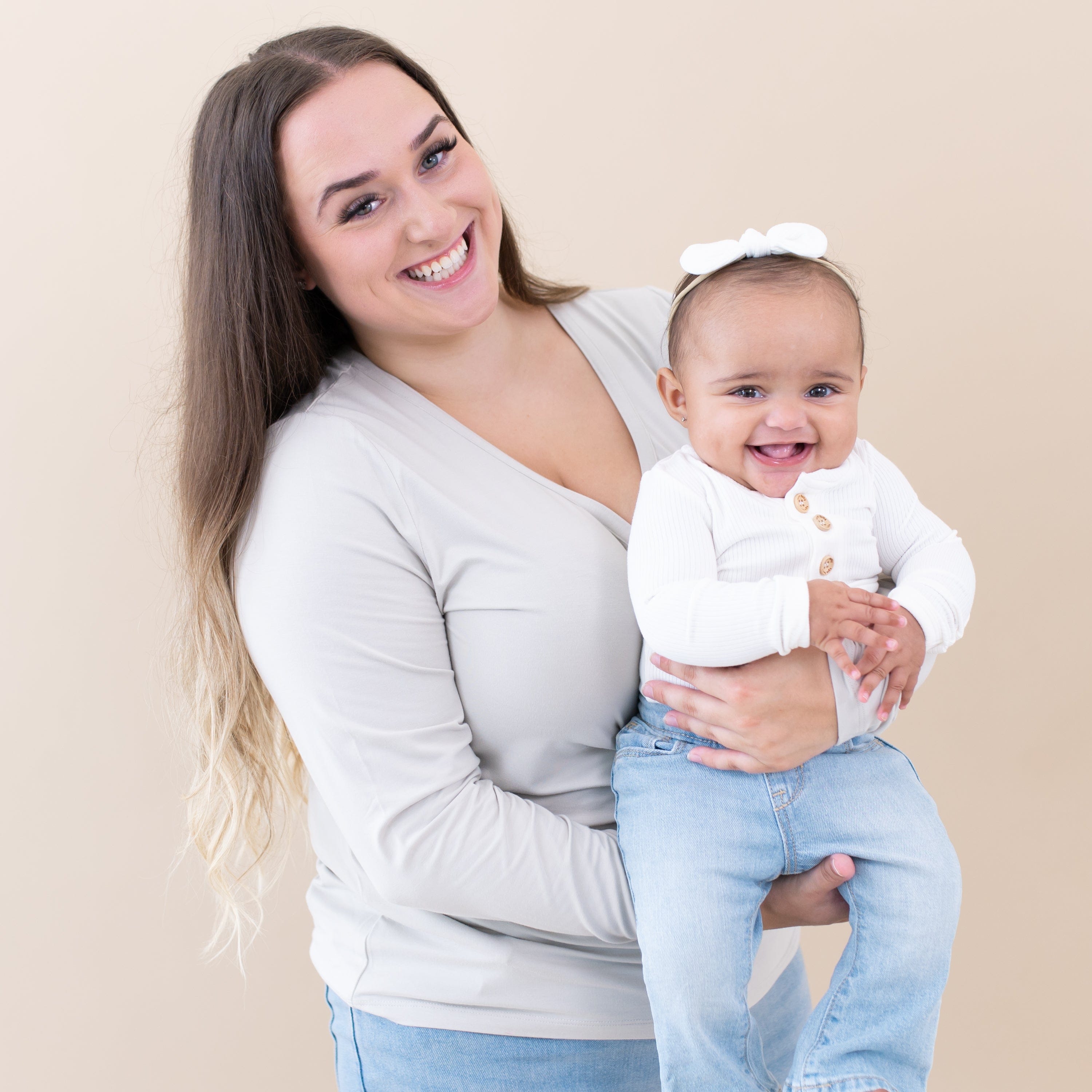 Smiling mom holding smiling infant wearing Kyte Baby Ribbed Long Sleeve Henley Bodysuit in Cloud white