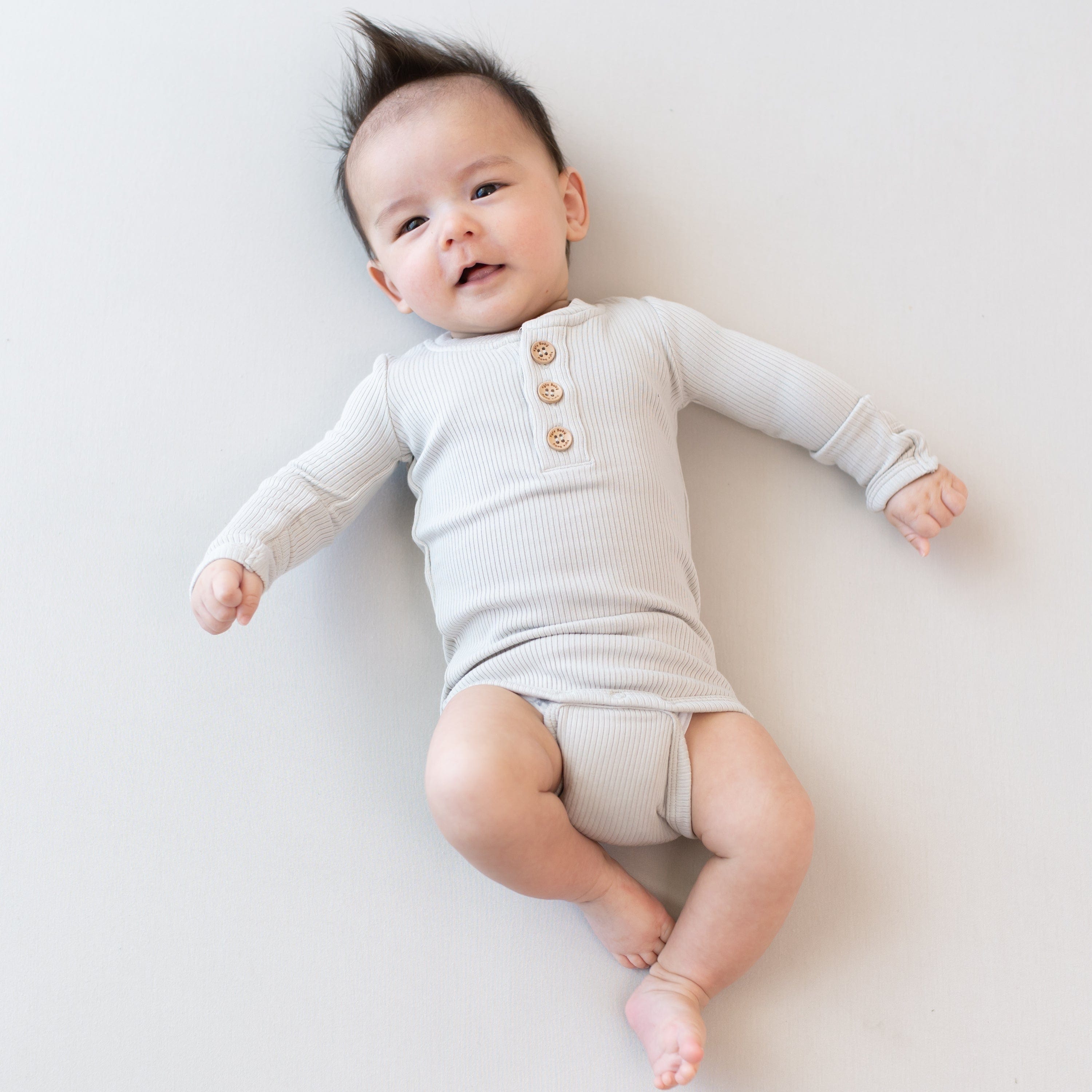 Infant wearing Kyte Baby Ribbed Long Sleeve Henley Bodysuit with snap closure in Oat