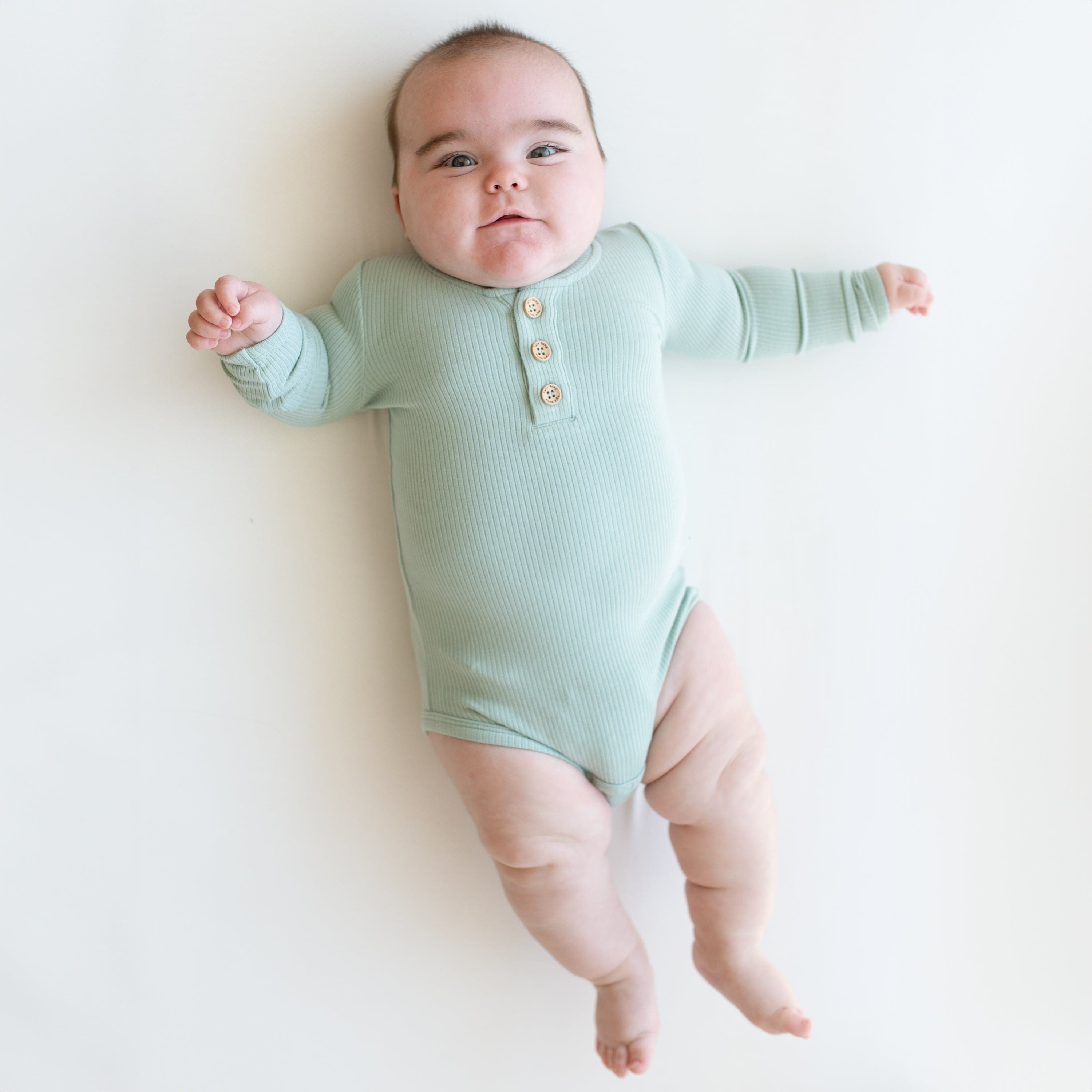 Infant wearing Kyte Baby Ribbed Long Sleeve Henley Bodysuit in Sage