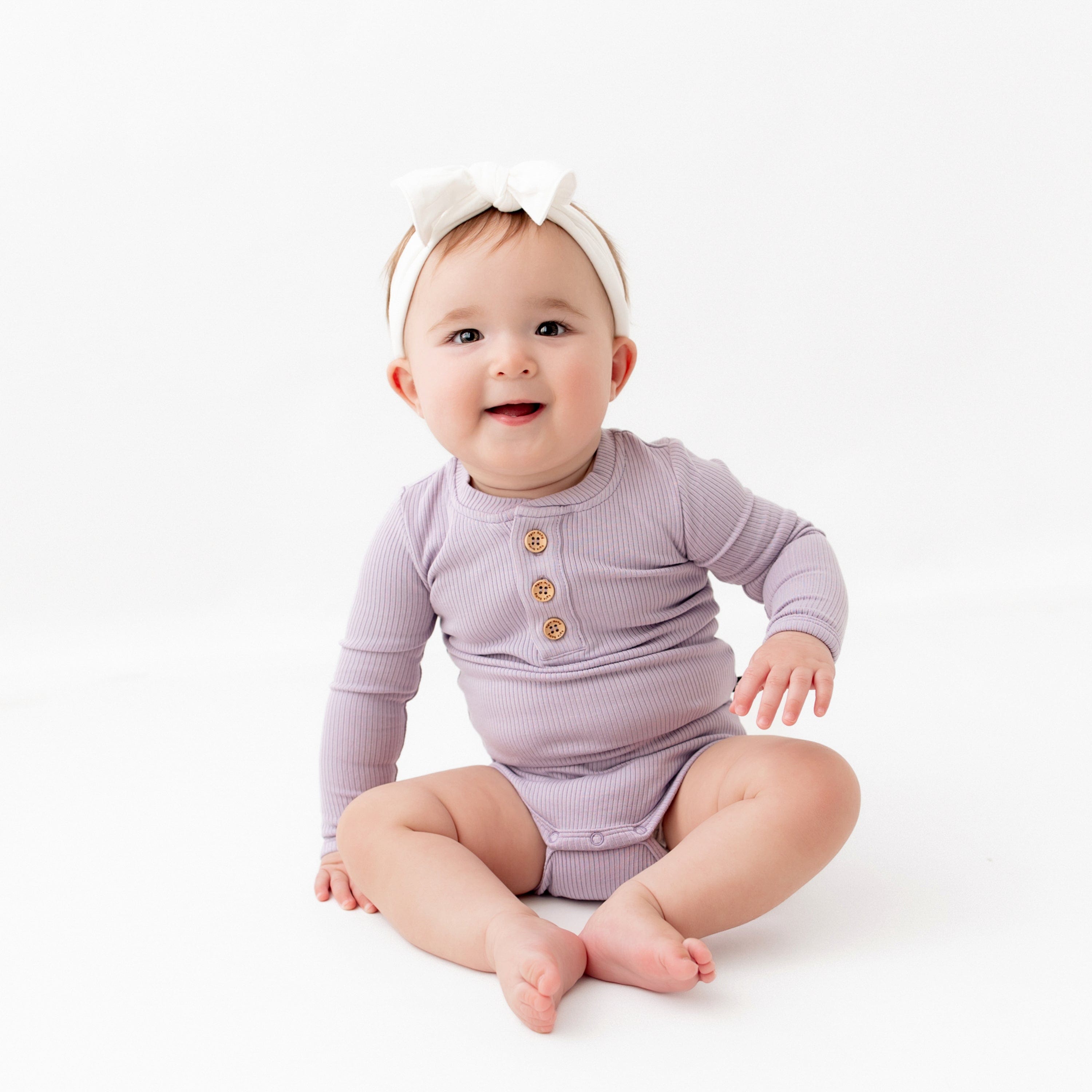 Infant wearing Kyte Baby Ribbed Long Sleeve Henley Bodysuit with snap closure in Taro purple