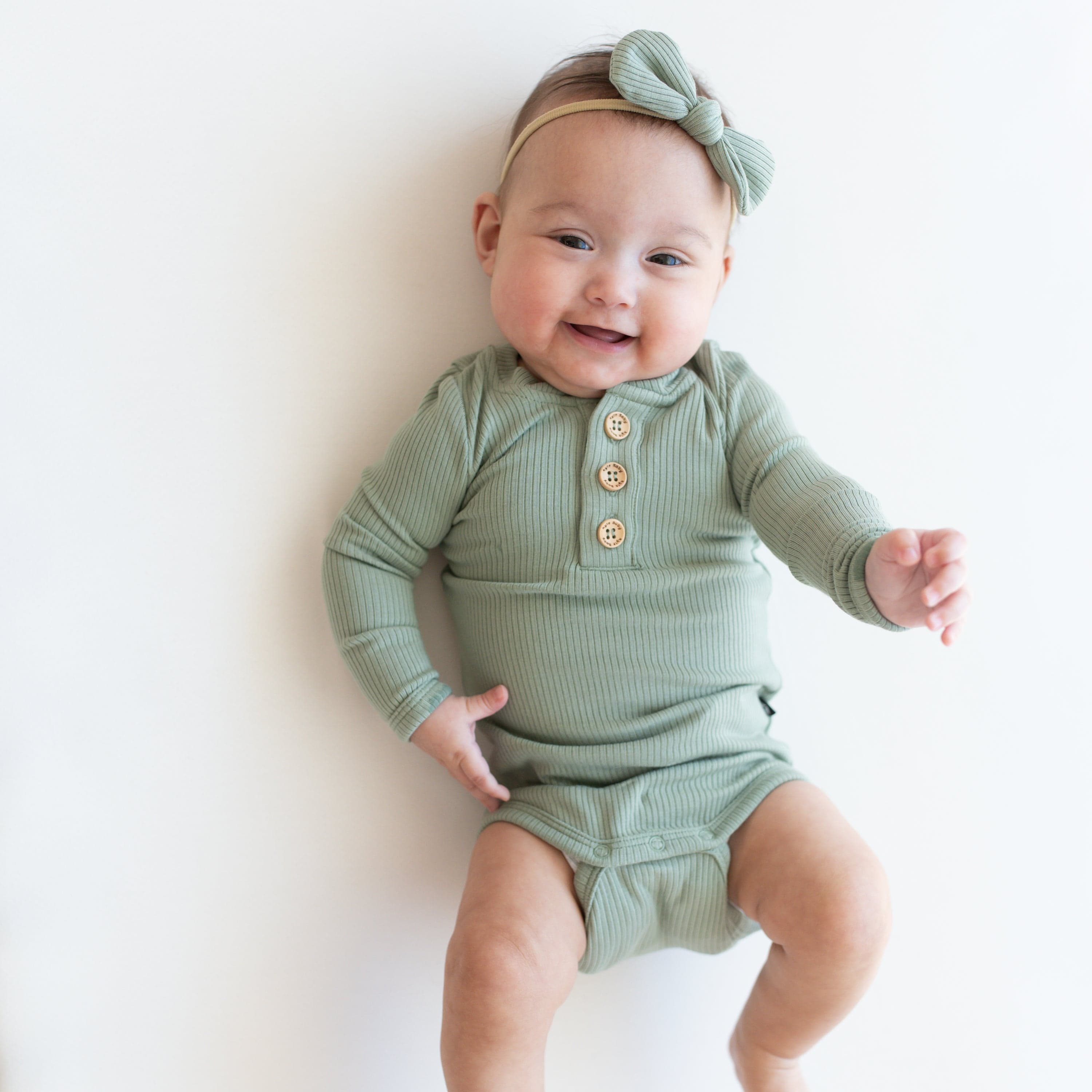 Infant wearing Kyte Baby Ribbed Long Sleeve Henley Bodysuit in Thyme