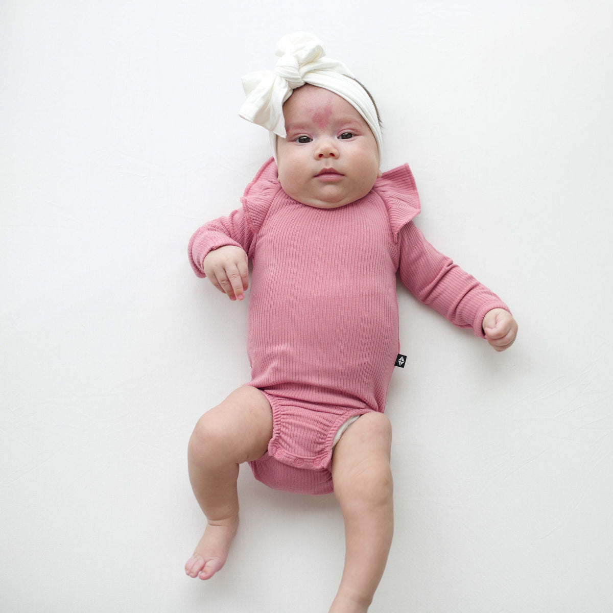 Infant wearing Kyte Baby bamboo Ribbed Long Sleeve Ruffle Leotard in Apple Blossom