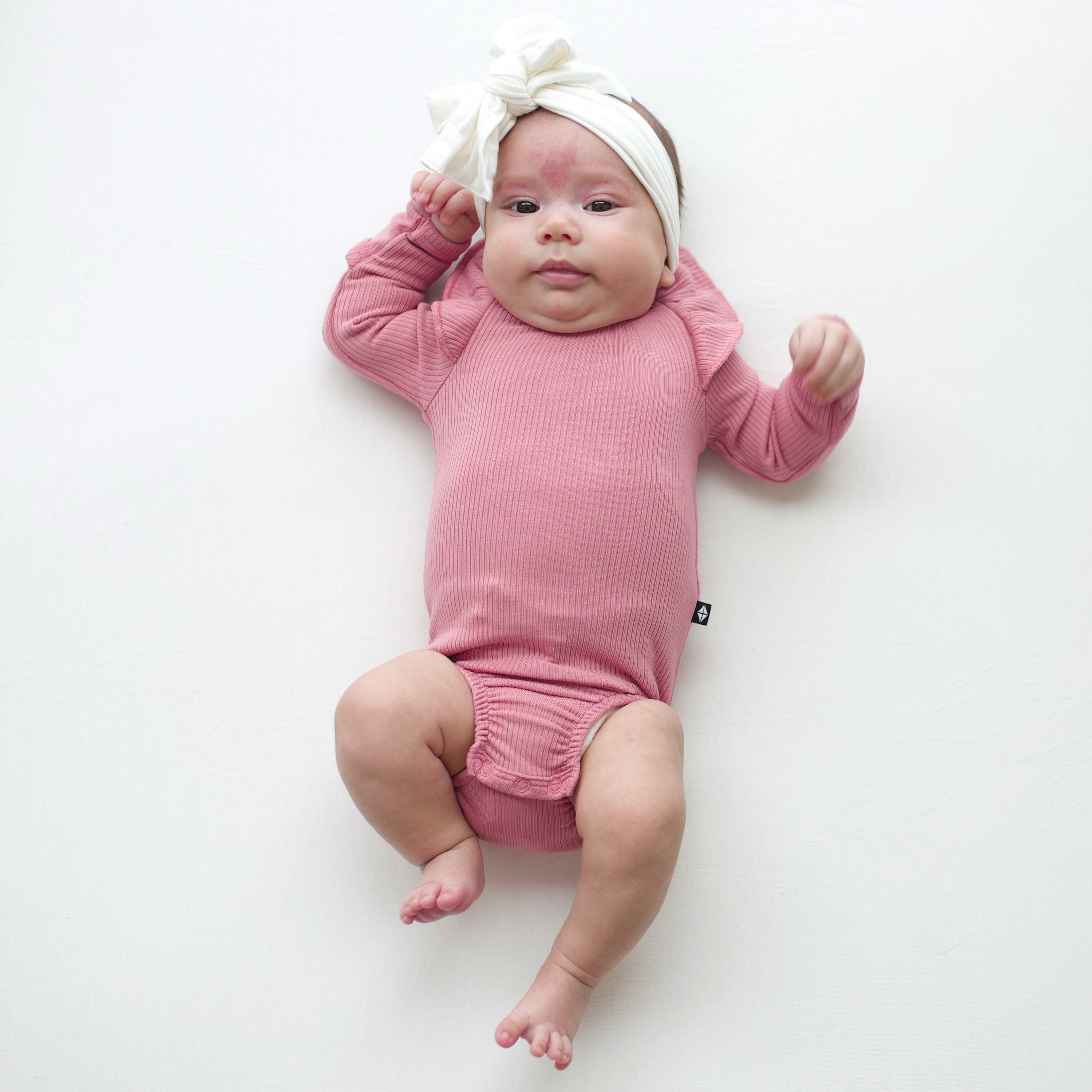 Newborn wearing Kyte Baby Ribbed Long Sleeve Ruffle Leotard in Apple Blossom pink