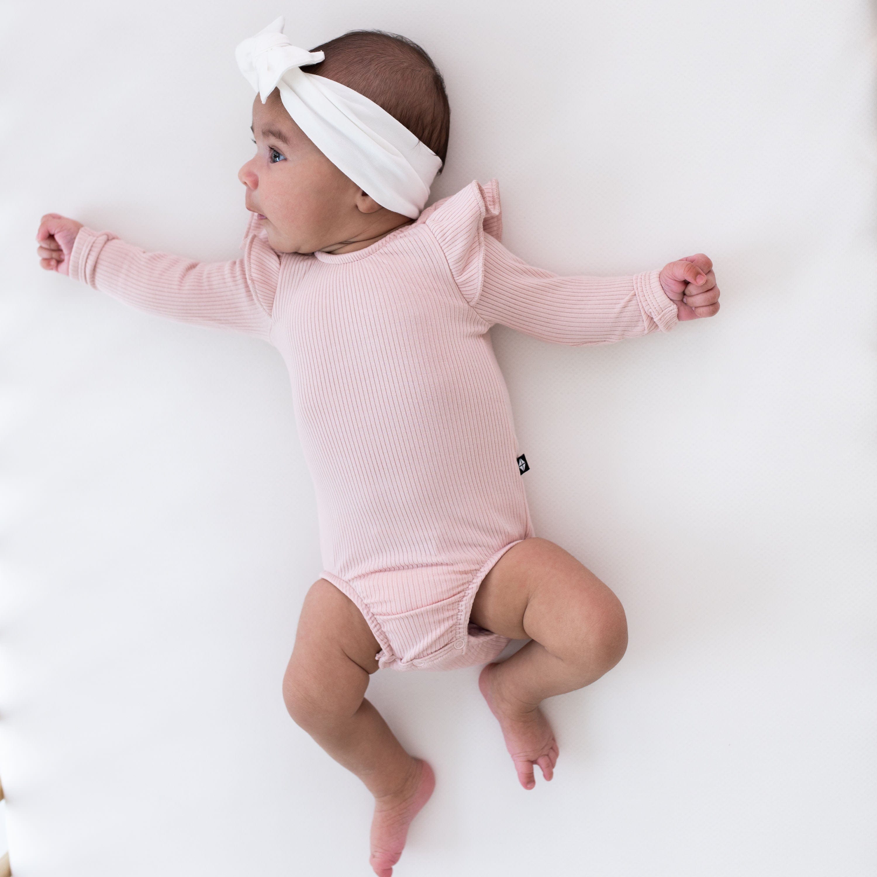 Newborn wearing Kyte Baby Ribbed Long Sleeve Ruffle Leotard in Blush Pink
