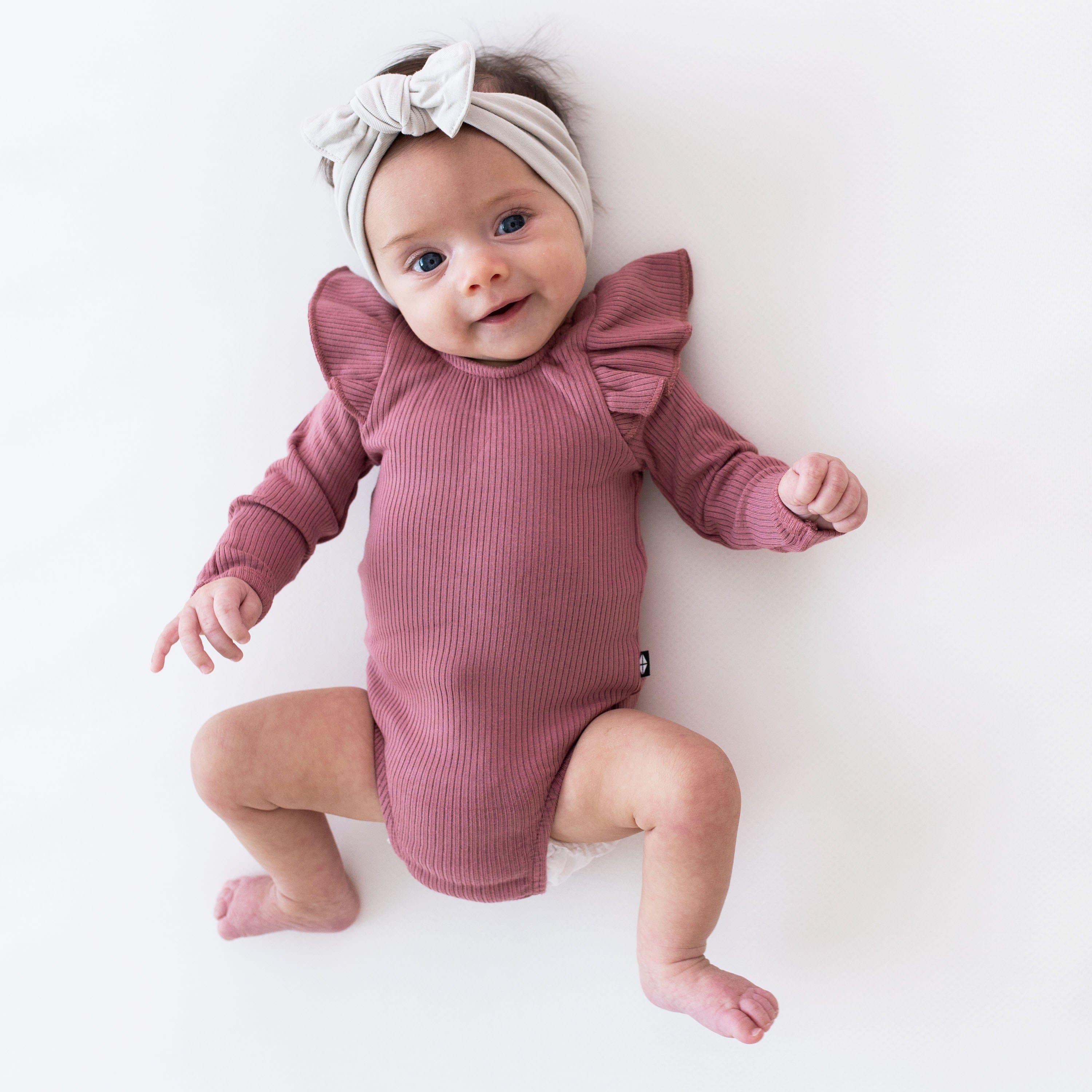 Infant wearing Kyte Baby bamboo Ribbed Long Sleeve Ruffle Leotard in Dusty Rose