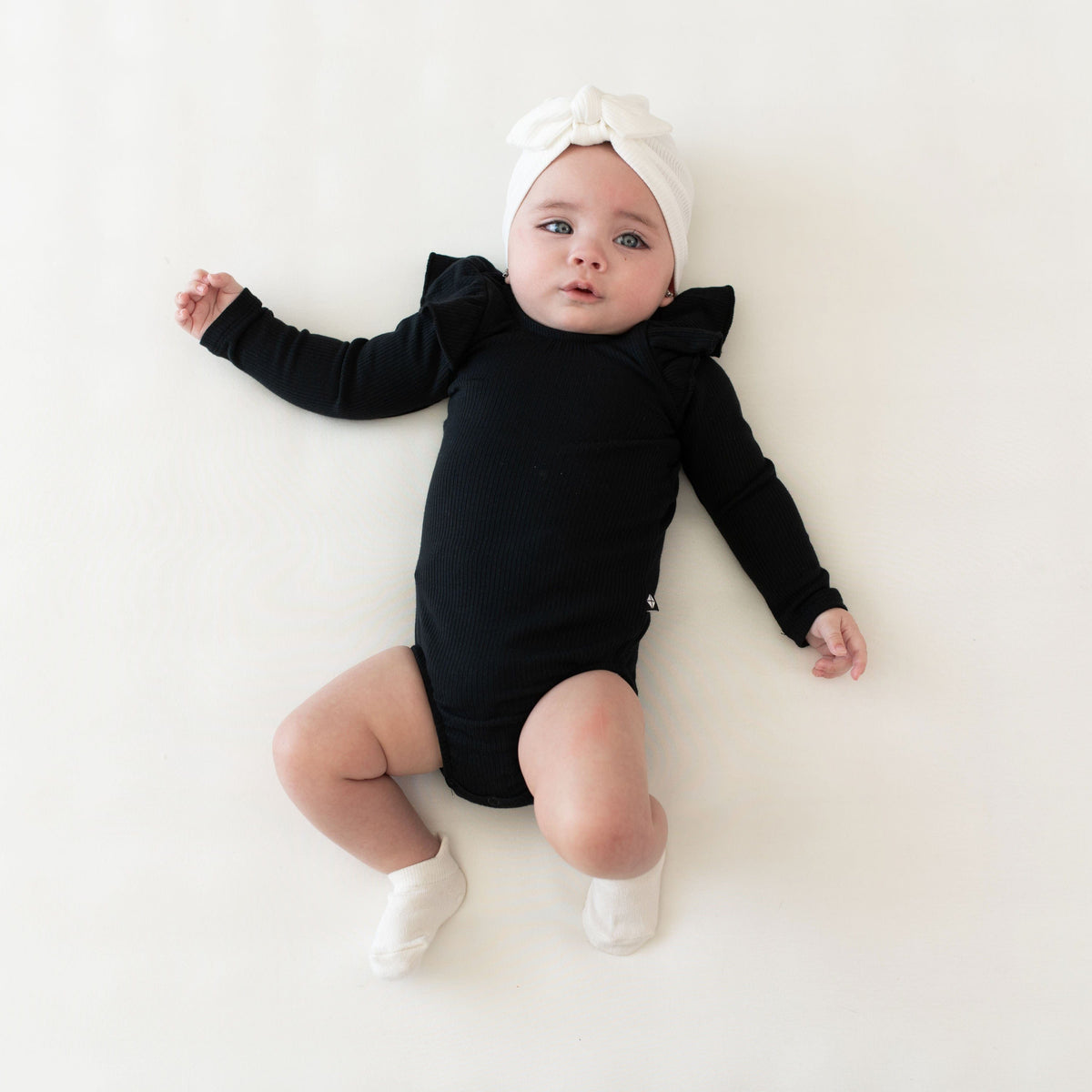 Infant wearing Kyte Baby bamboo Ribbed Long Sleeve Ruffle Leotard in Midnight
