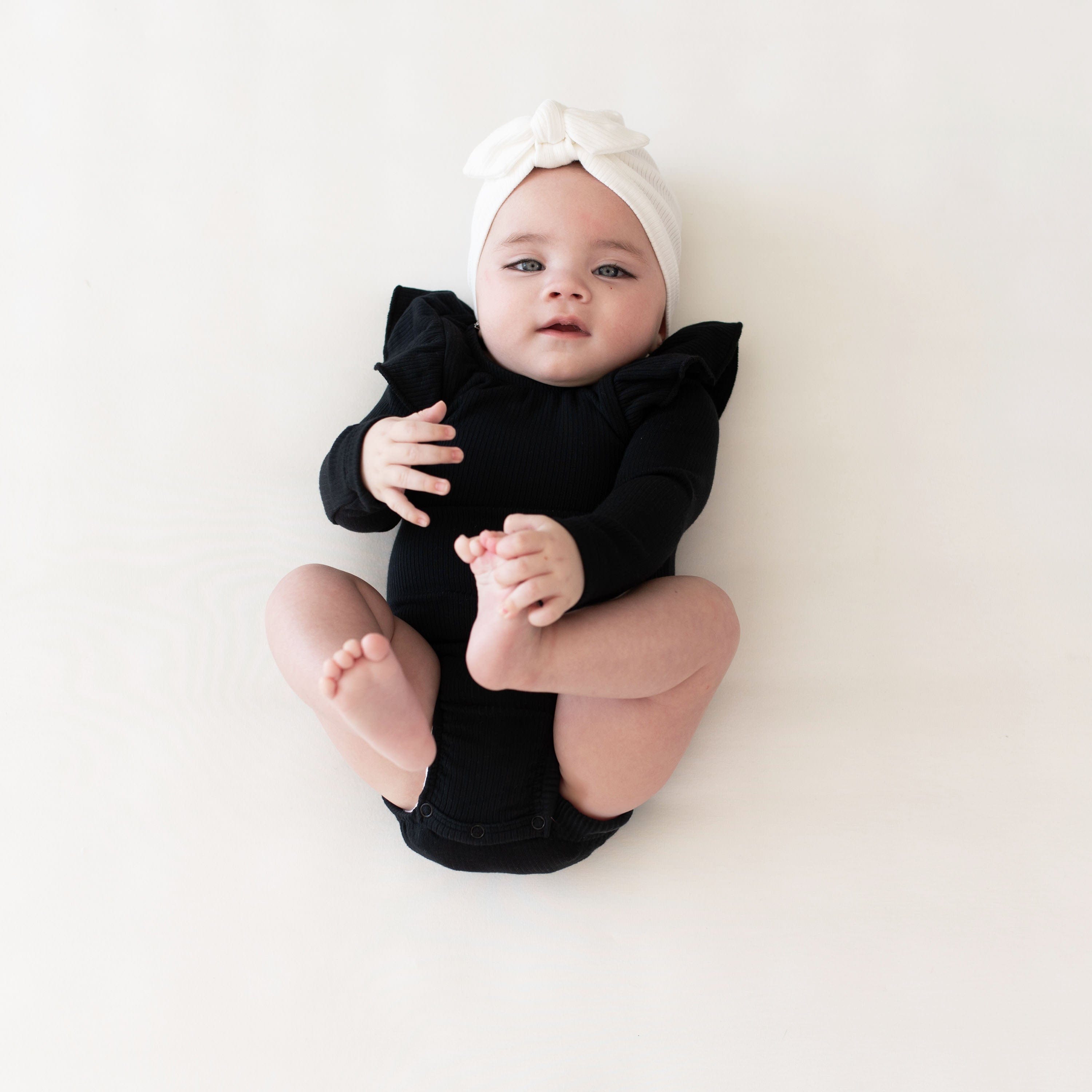 Infant wearing Kyte Baby Ribbed Long Sleeve Ruffle Leotard in Midnight Black