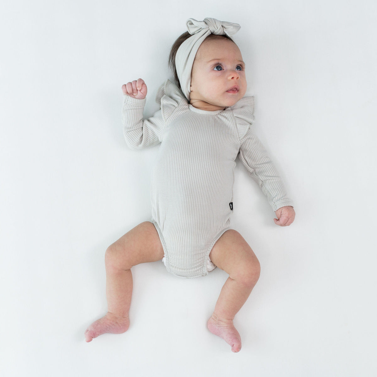 Newborn wearing Kyte Baby Ribbed Long Sleeve Ruffle Leotard in Oat