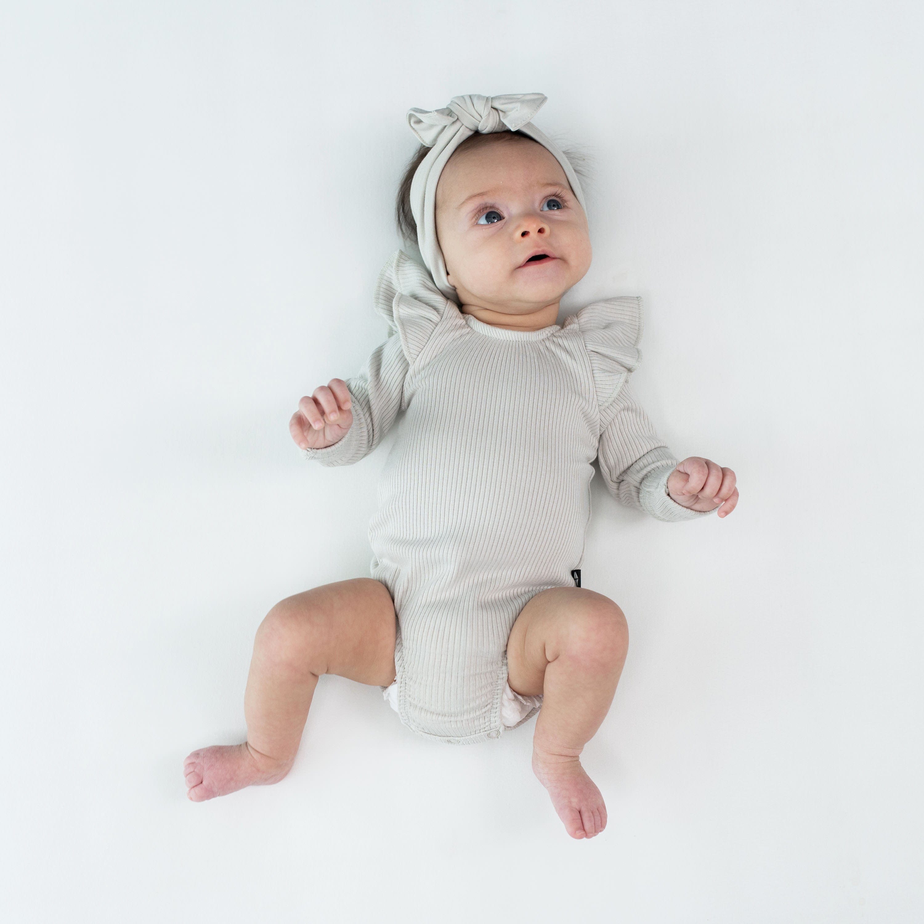 Infant wearing Kyte Baby bamboo Ribbed Long Sleeve Ruffle Leotard in Oat