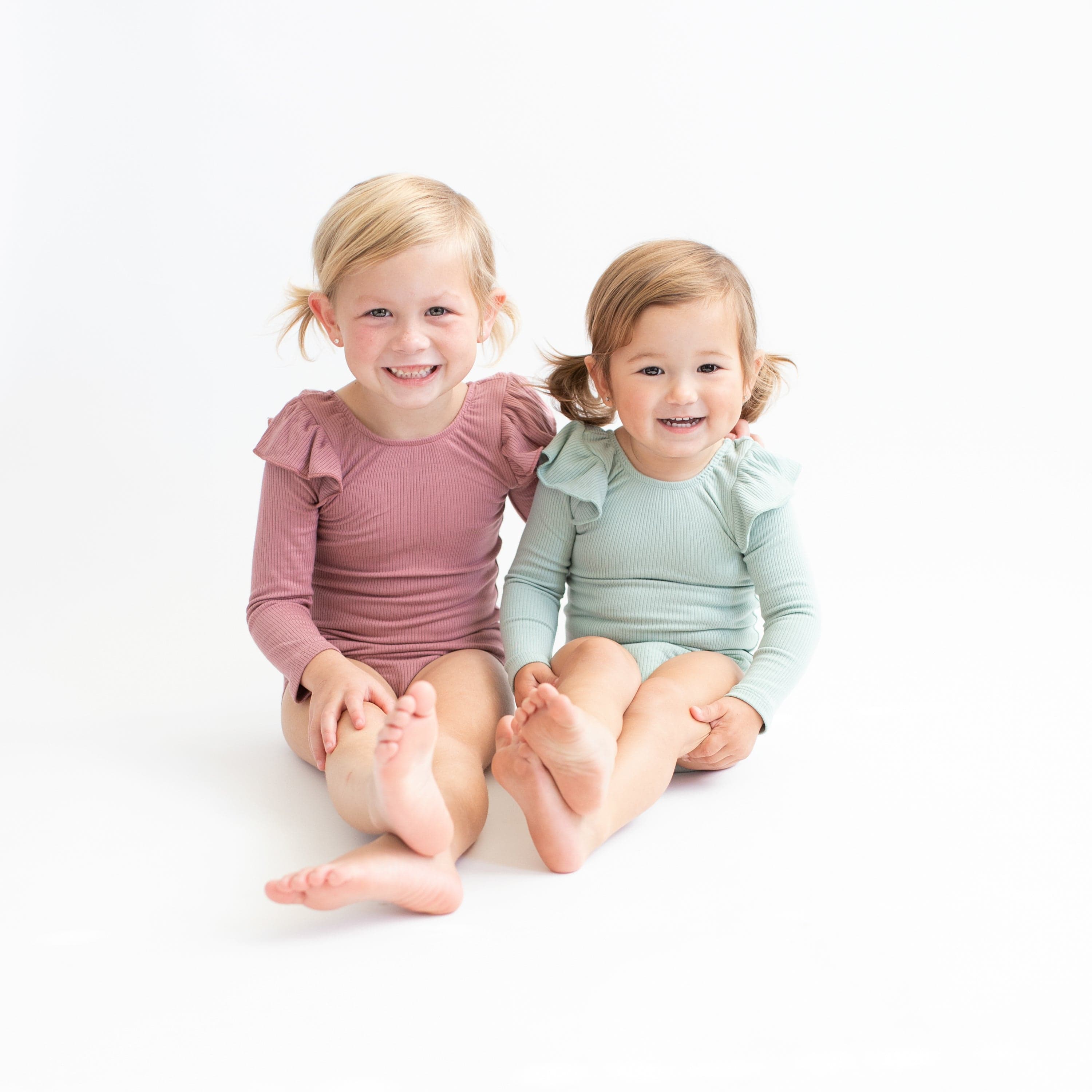Girls wearing Kyte Baby Bamboo Ribbed Long Sleeve Ruffle Leotards