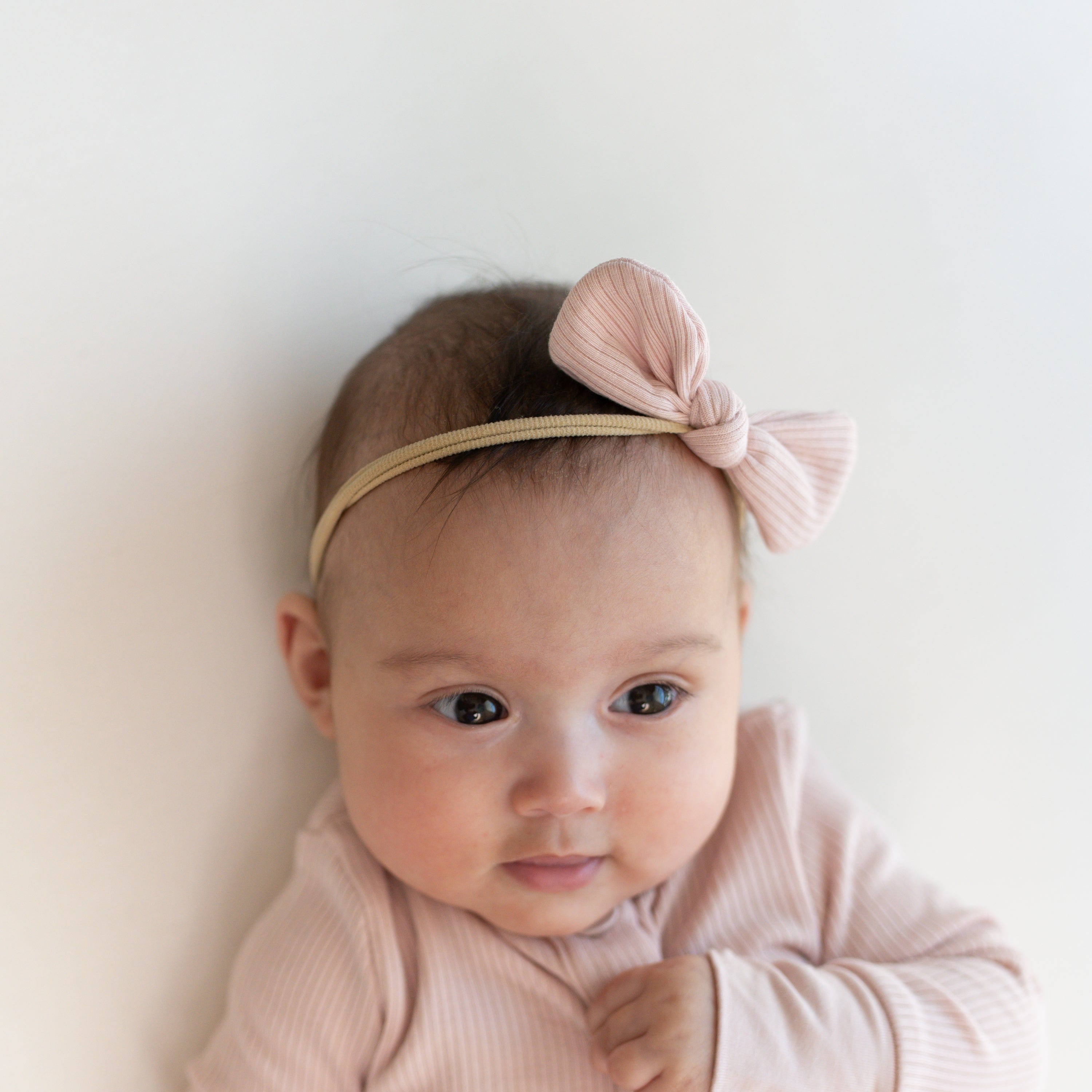 Infant wearing Kyte Baby Ribbed Bow with Nylon Band in Blush pink