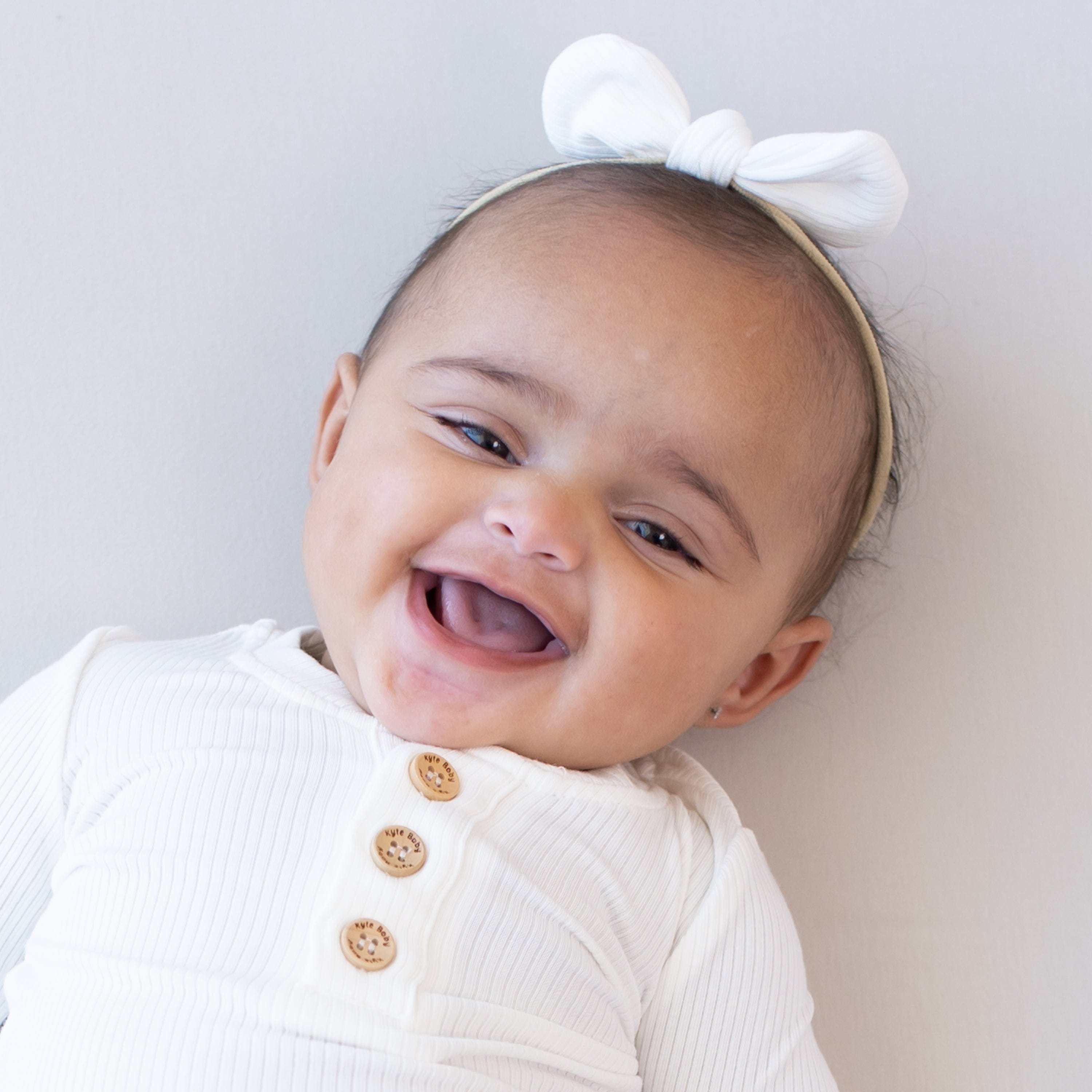 Close up of smiling baby wearing Kyte Baby Ribbed Nylon Bow Cloud and Ribbed Henley top with wooden buttons