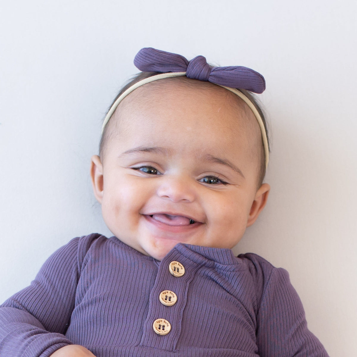 Infant wearing Kyte Baby Ribbed Nylon Bow in Currant