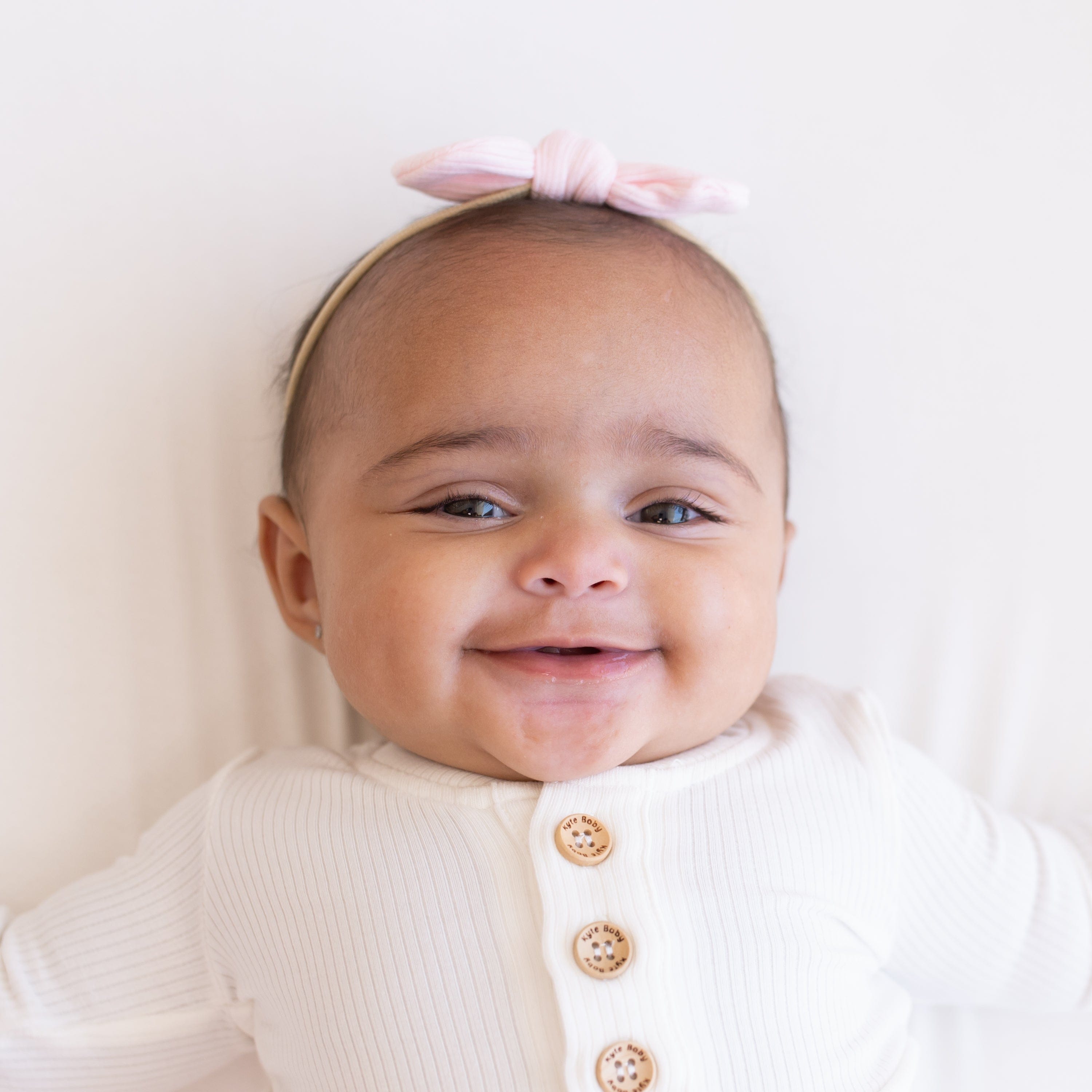 Infant wearing Kyte Baby Ribbed Bow with Nylon Band in Sakura