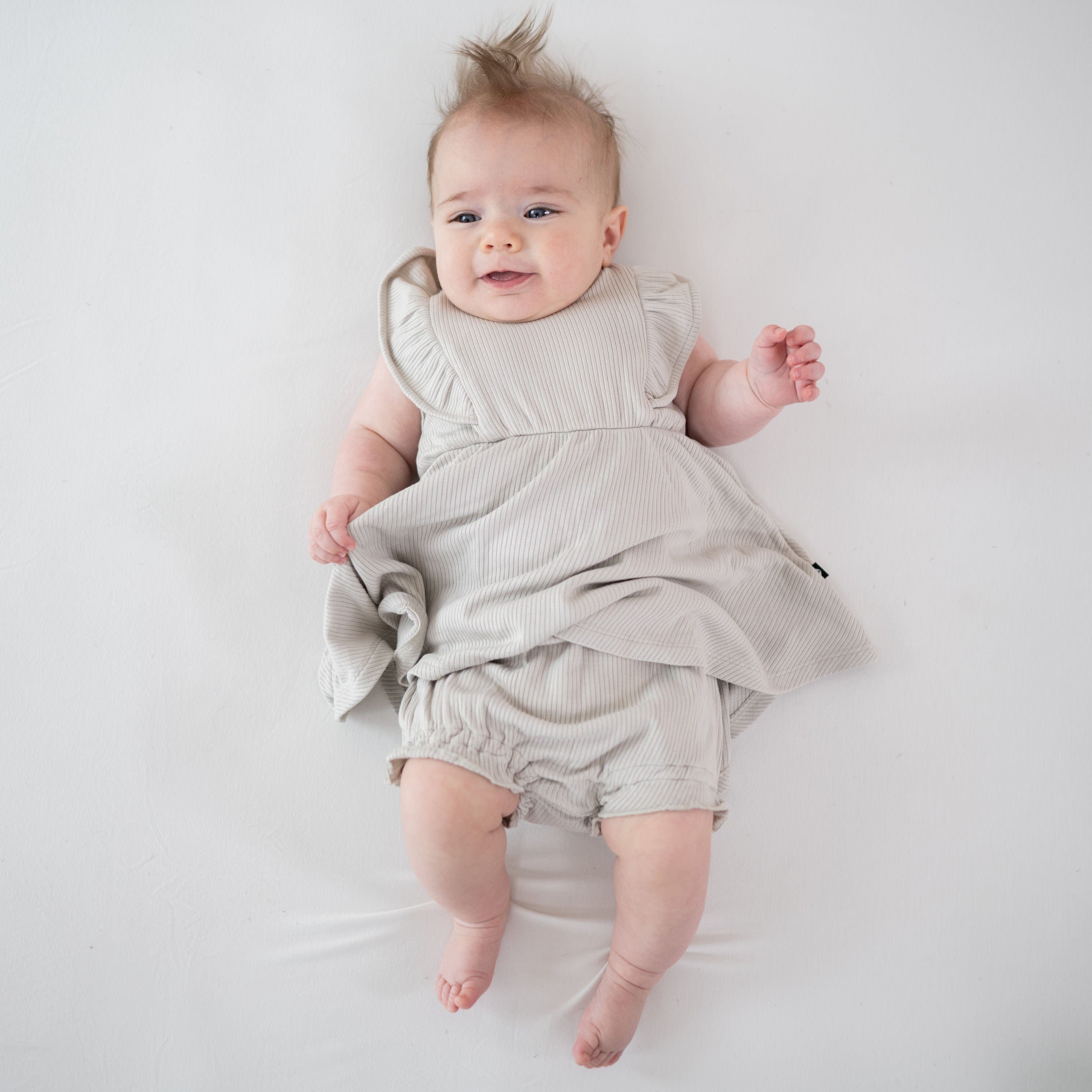 Infant wearing Kyte Baby Ribbed Peplum Dress Set with Flutter Sleeves in Oat