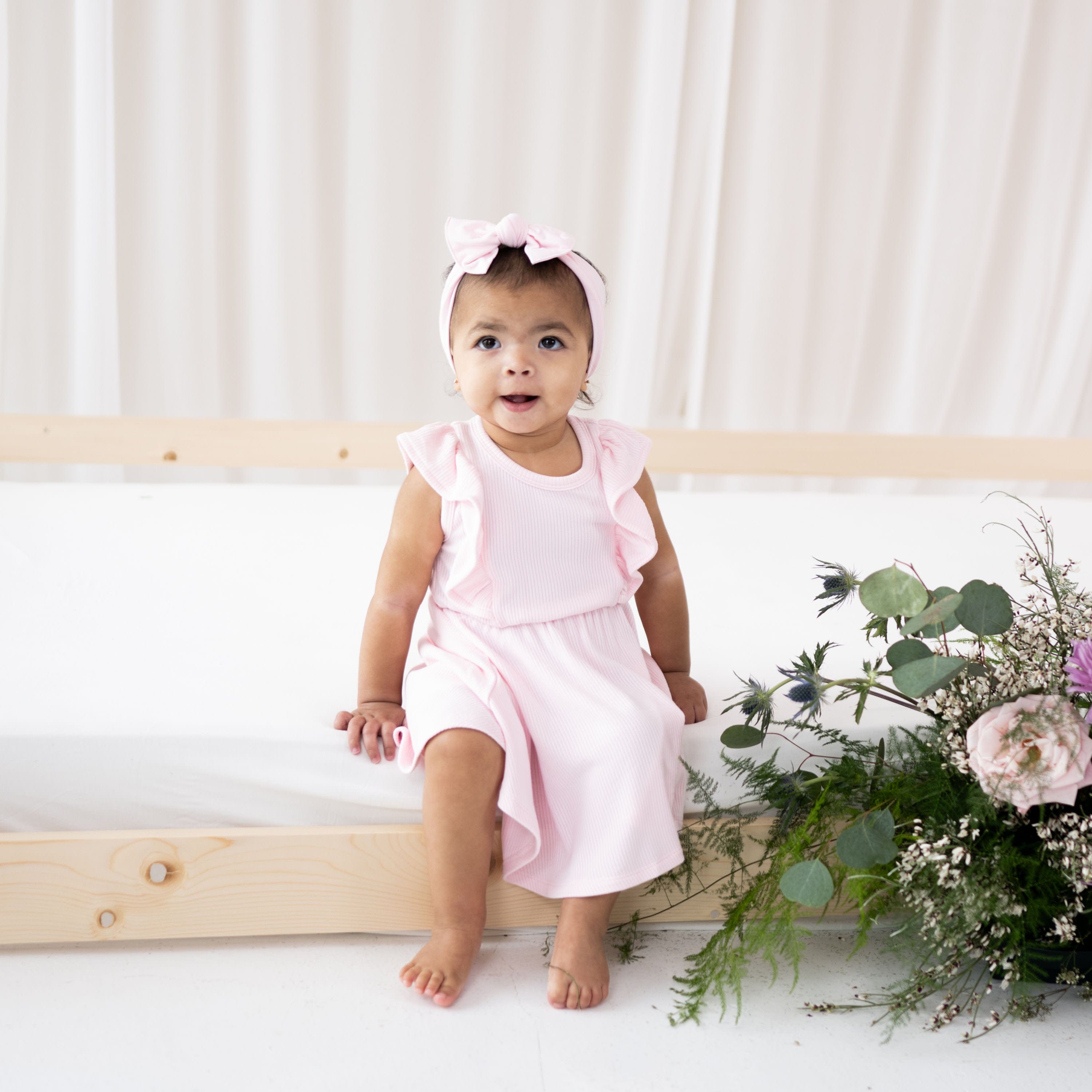Child wearing Kyte Baby Bamboo Ribbed Peplum Dress Set in Sakura pink with matching bow