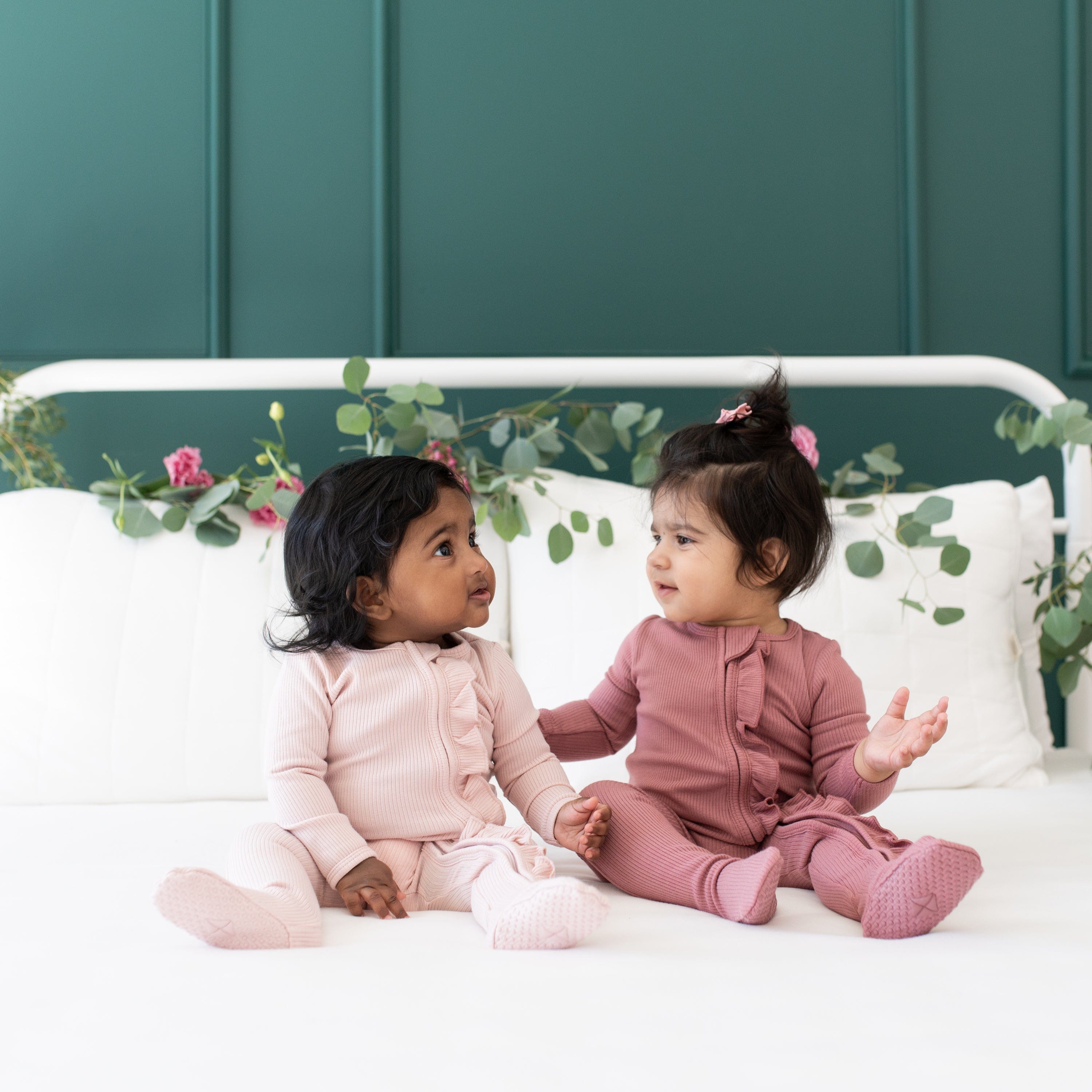 Babies wearing Kyte Baby Bamboo Ribbed Zippered Footie pajamas with Ruffle