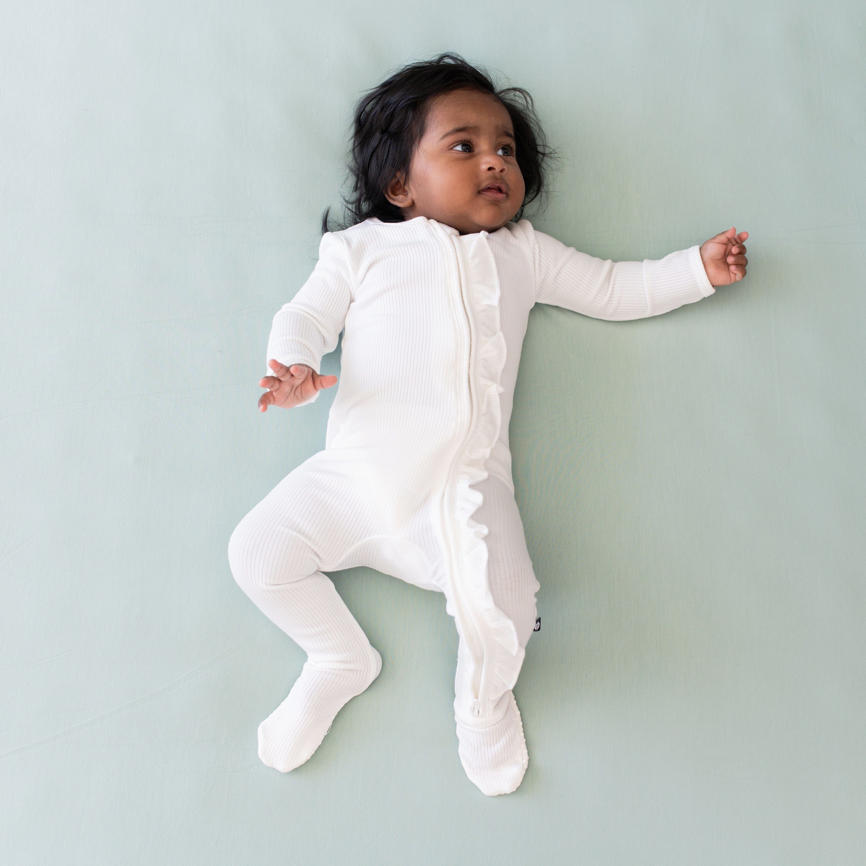 Infant wearing Kyte Baby Ribbed Ruffle Zipper Footie in Cloud