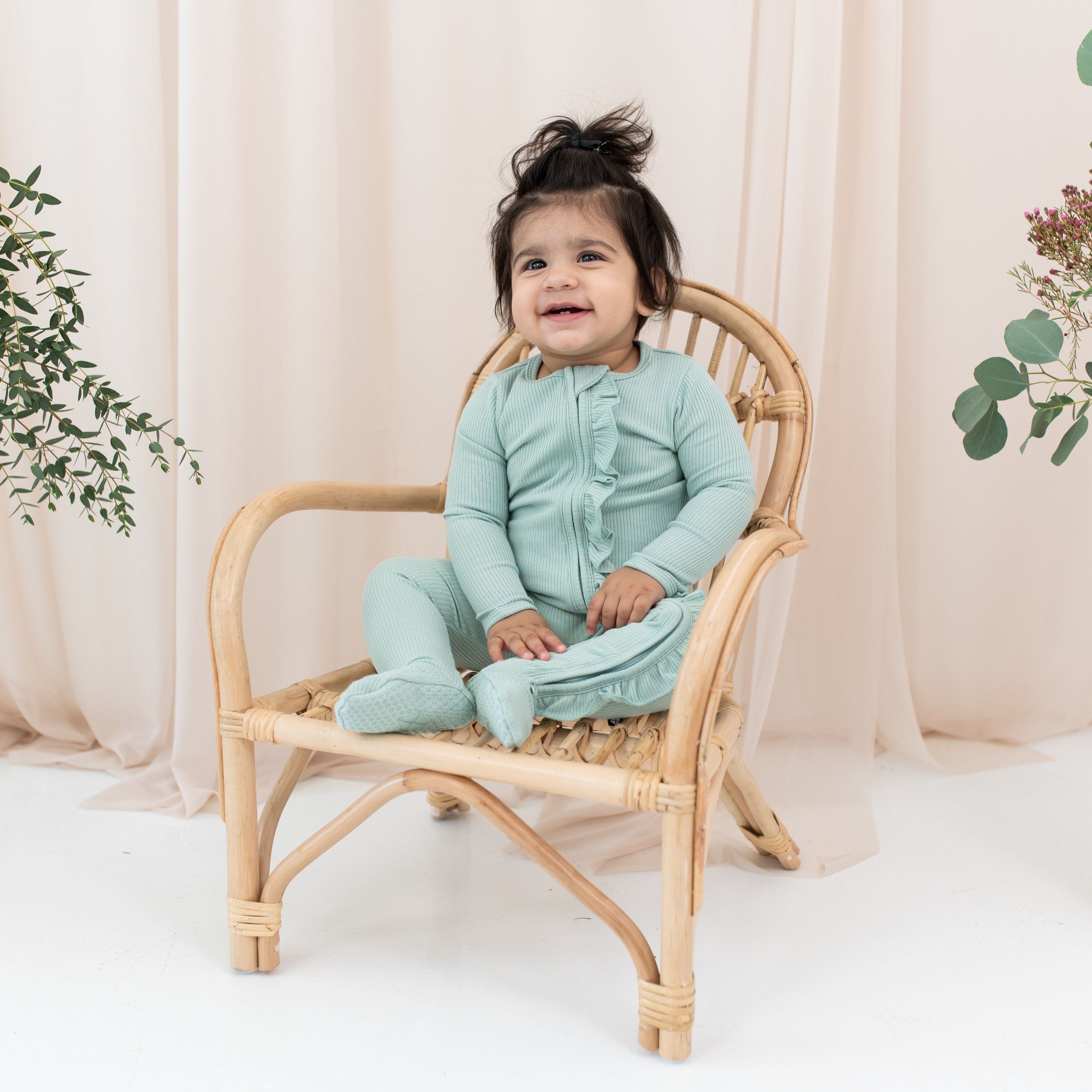Toddler wearing Kyte Baby Ribbed Ruffle Zipper Footie in Sage green