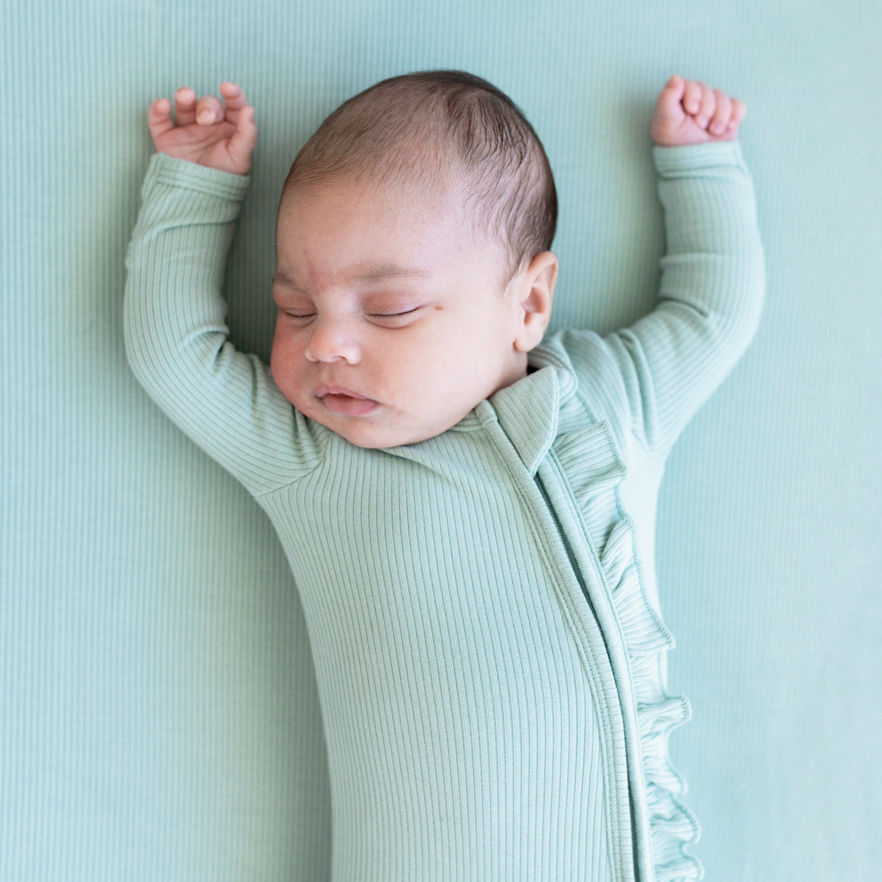 Infant wearing Kyte Baby Ribbed Zipper Footie with Ruffle in Sage