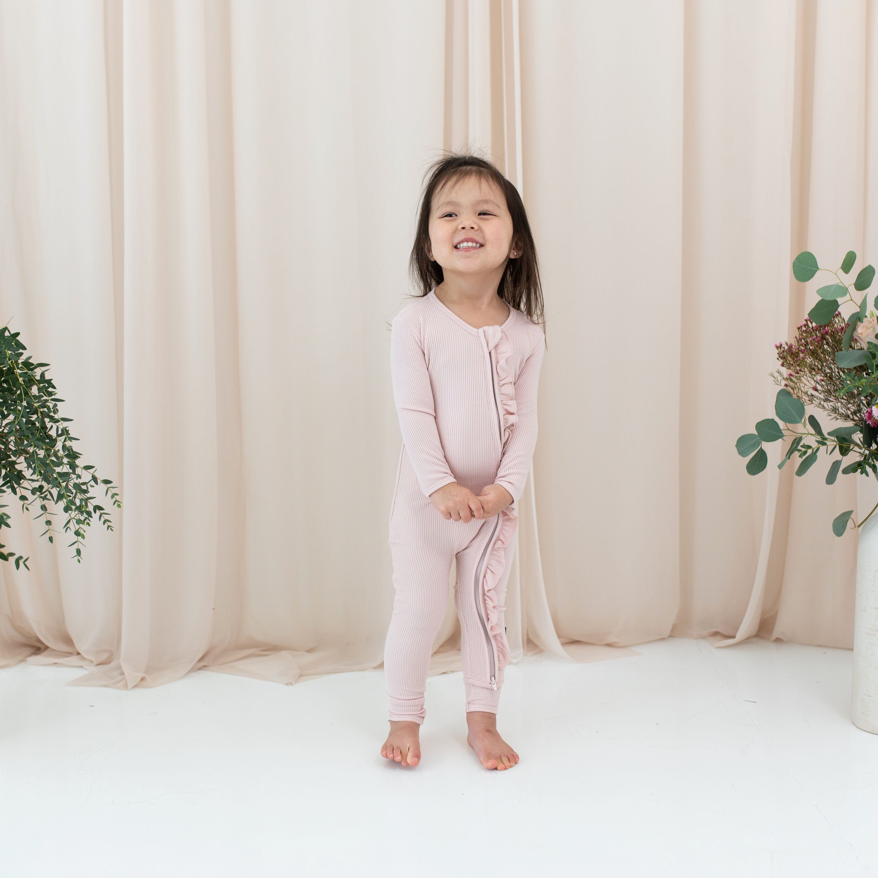 Toddler wearing Kyte Baby Ribbed Zipper Romper with Ruffle in Blush pink