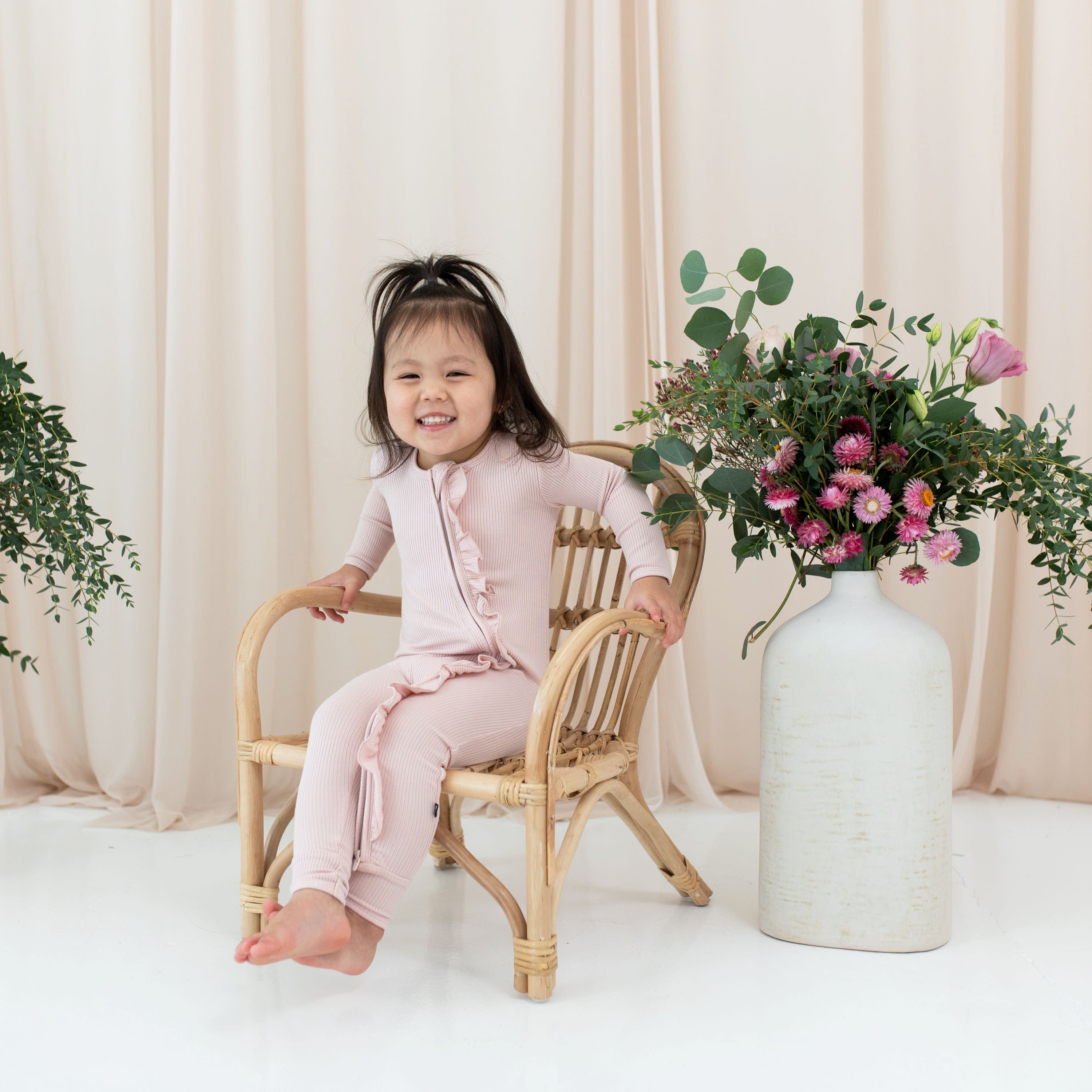 Toddler wearing Kyte Baby Ribbed Ruffle Zipper Romper in Blush pink
