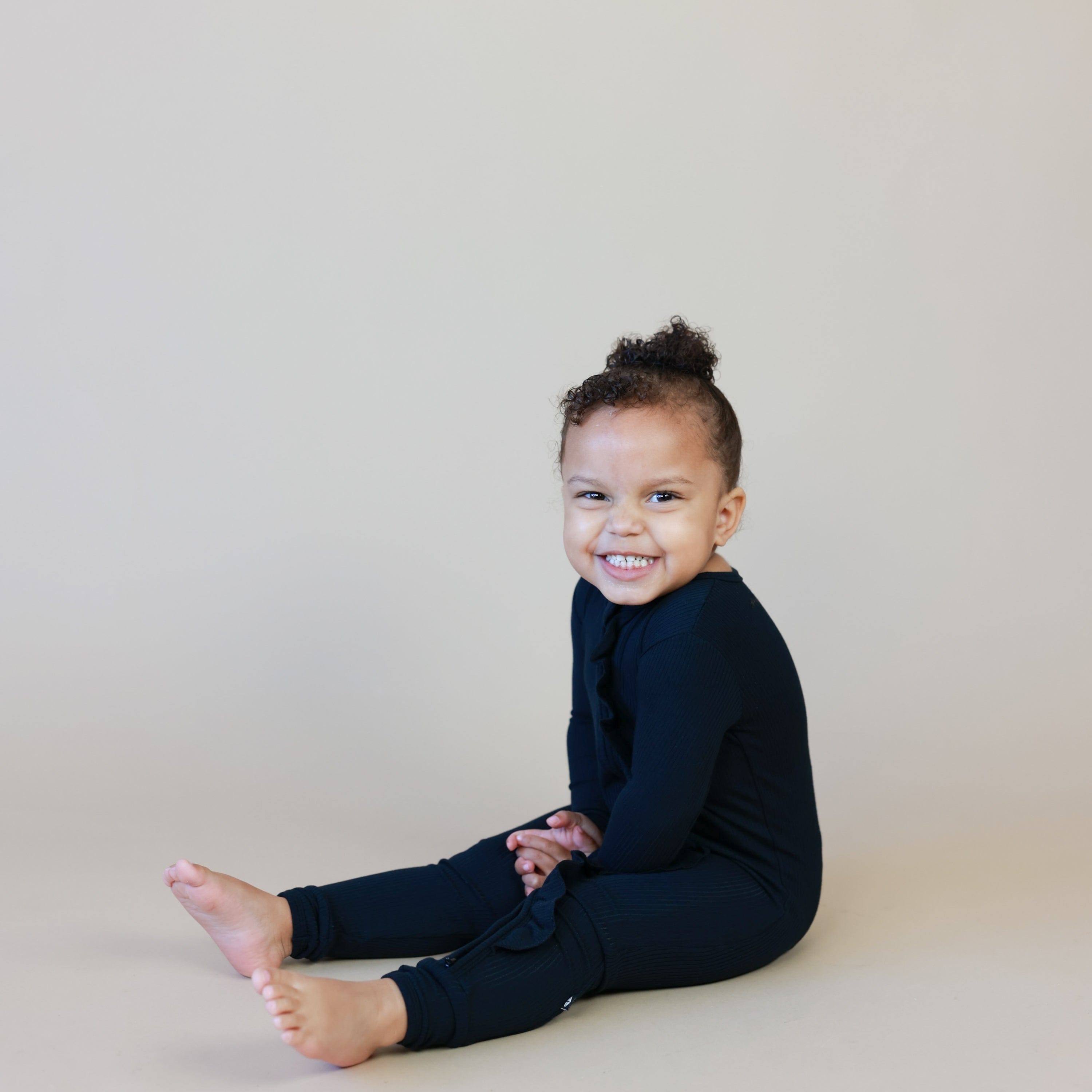 Toddler wearing Kyte Baby Ribbed Zipper Romper with Ruffle in Midnight black