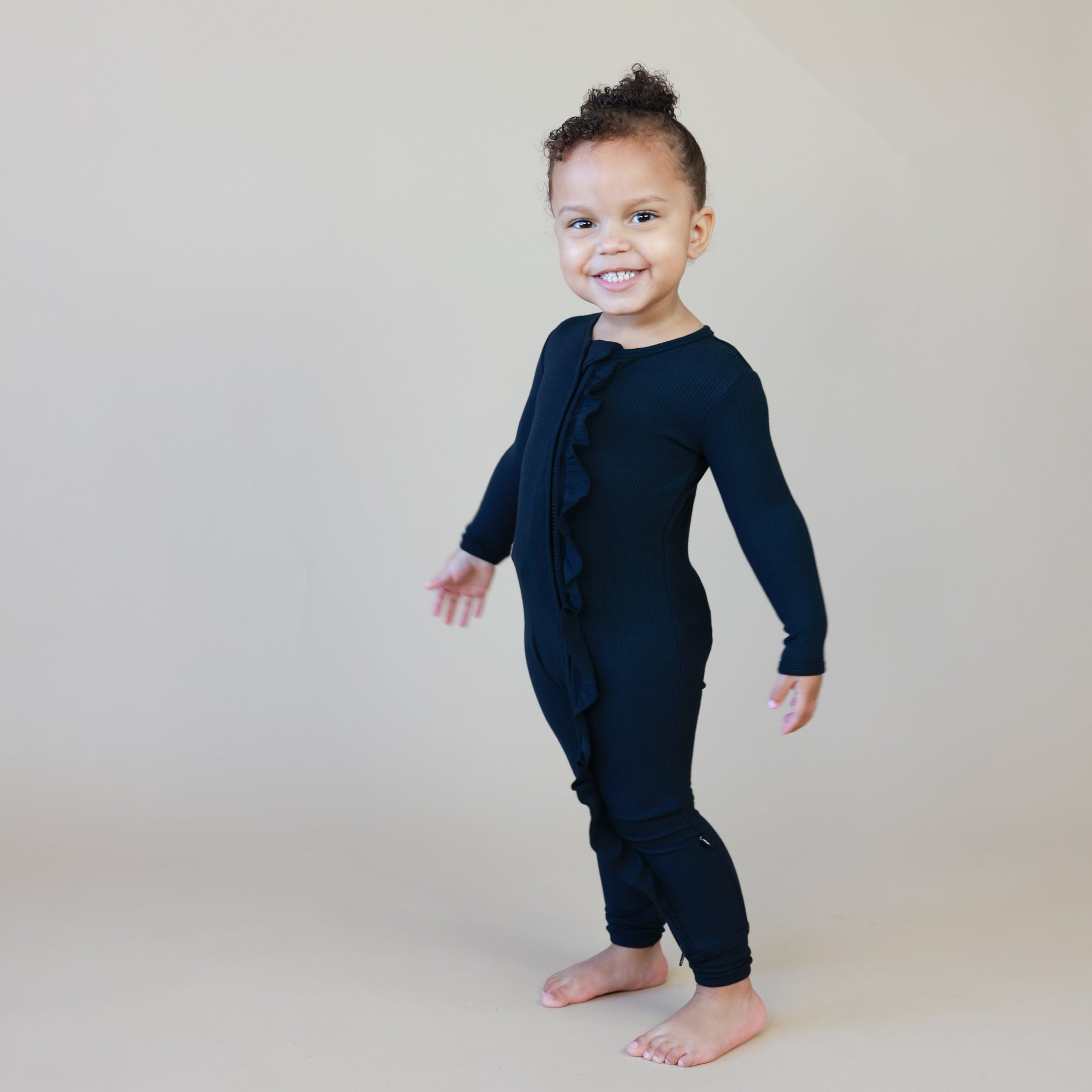 Girl wearing Kyte Baby bamboo Ribbed Ruffle Zipper Romper in Midnight black