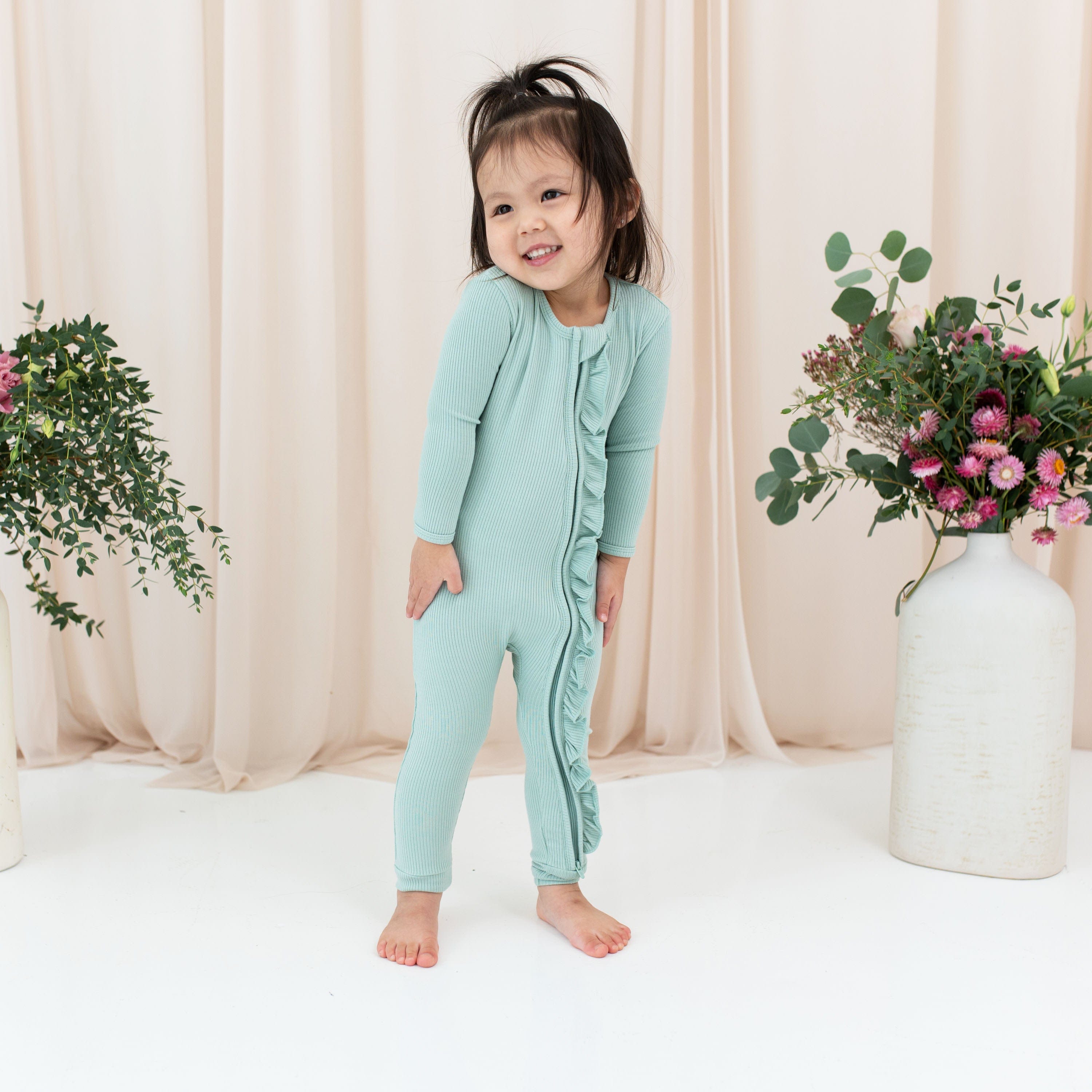 Toddler wearing Kyte Baby Ribbed Ruffle Zipper Romper in Sage