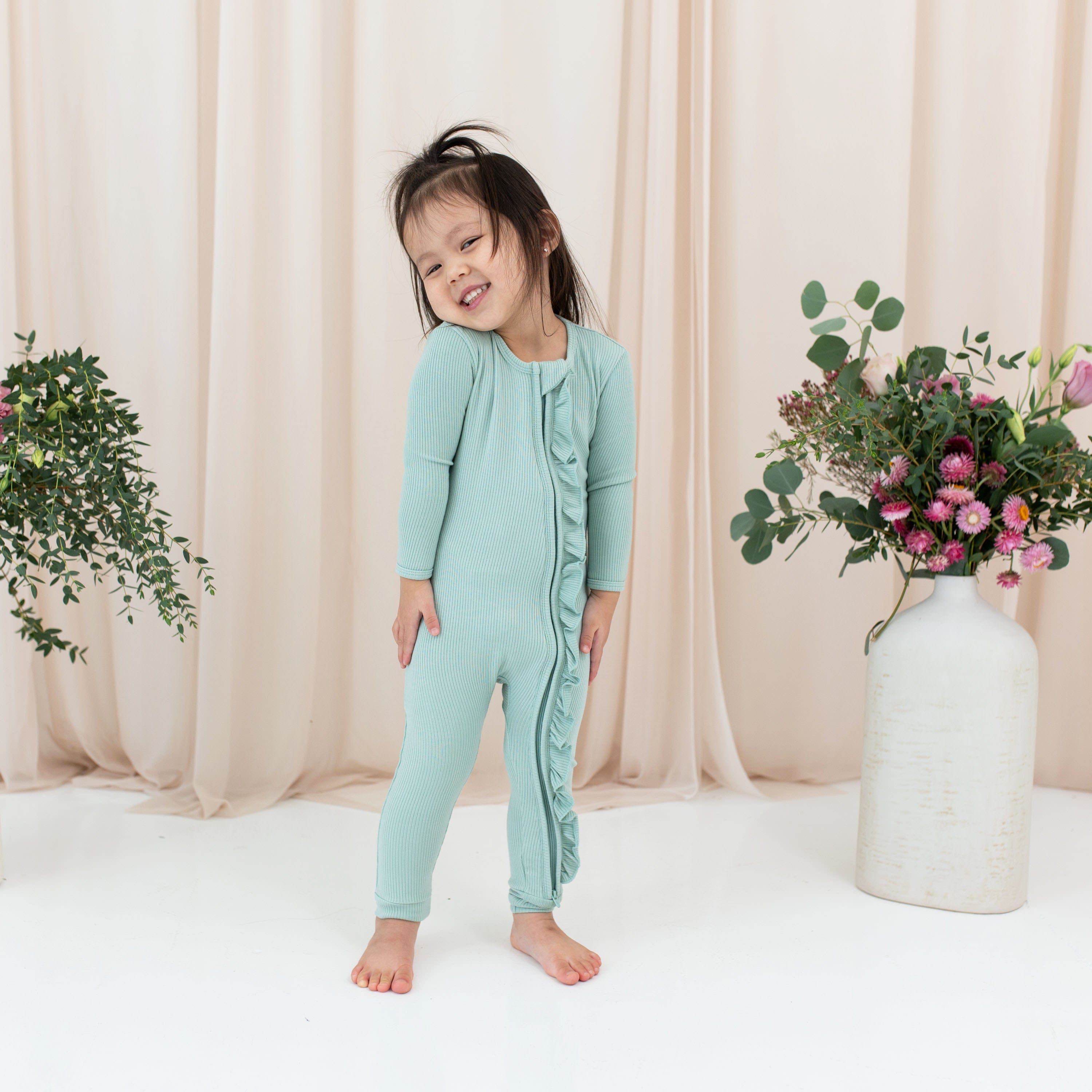 Toddler wearing Kyte Baby Ribbed Zipper Romper with Ruffle in Sage