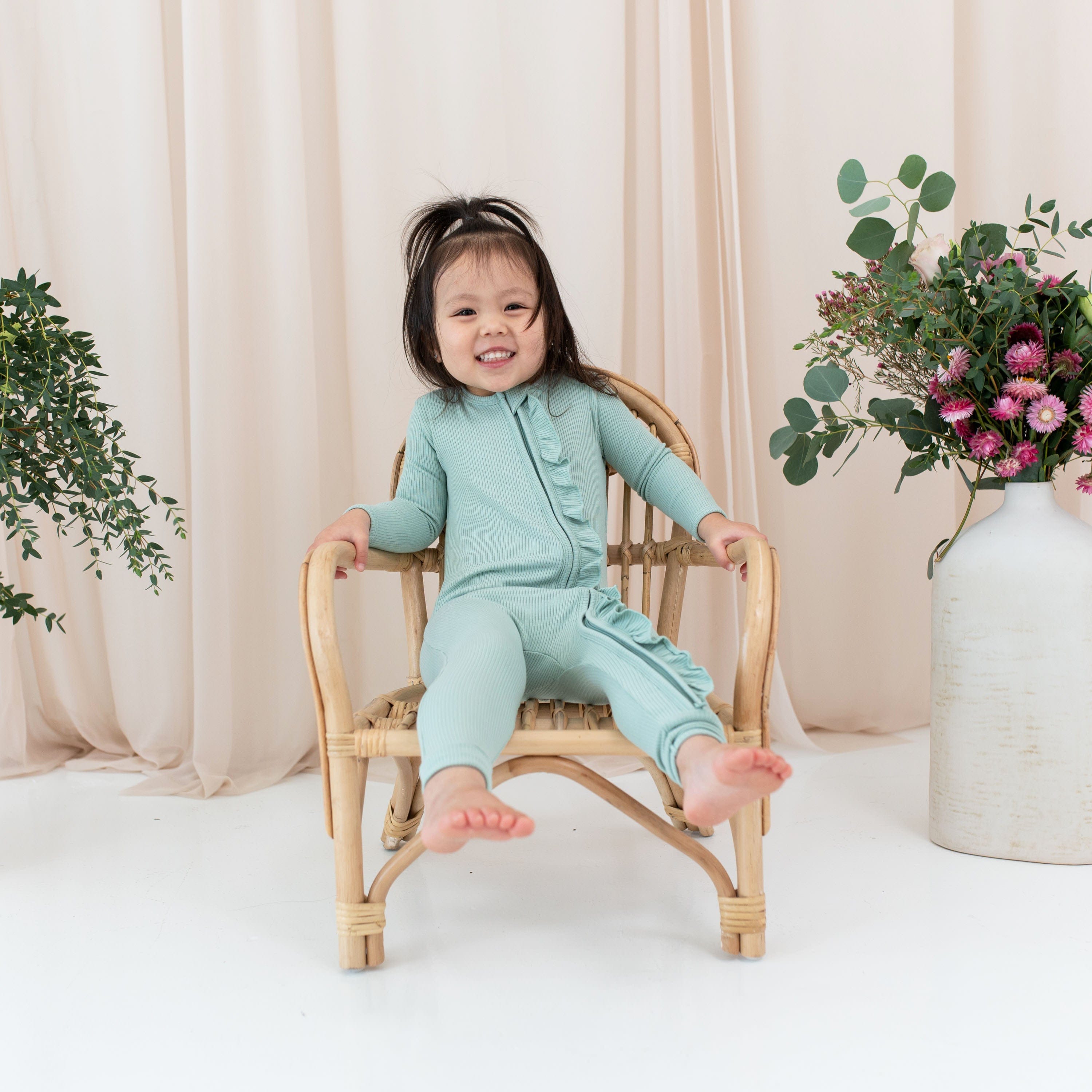 Girl wearing Kyte Baby bamboo Ribbed Ruffle Zipper Romper in Sage