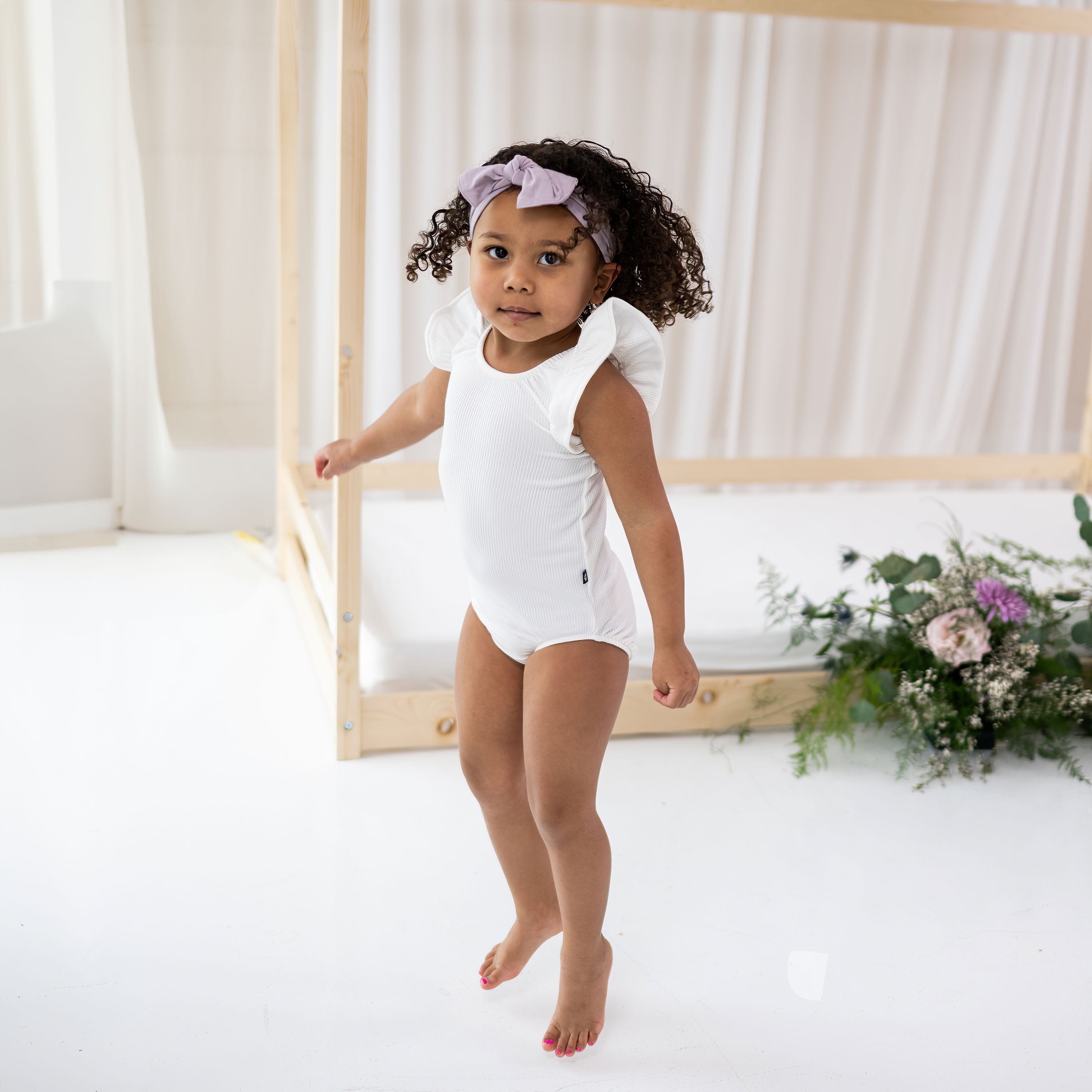 Child wearing Kyte Baby bamboo Ribbed Sleeveless Ruffle Leotard in Cloud