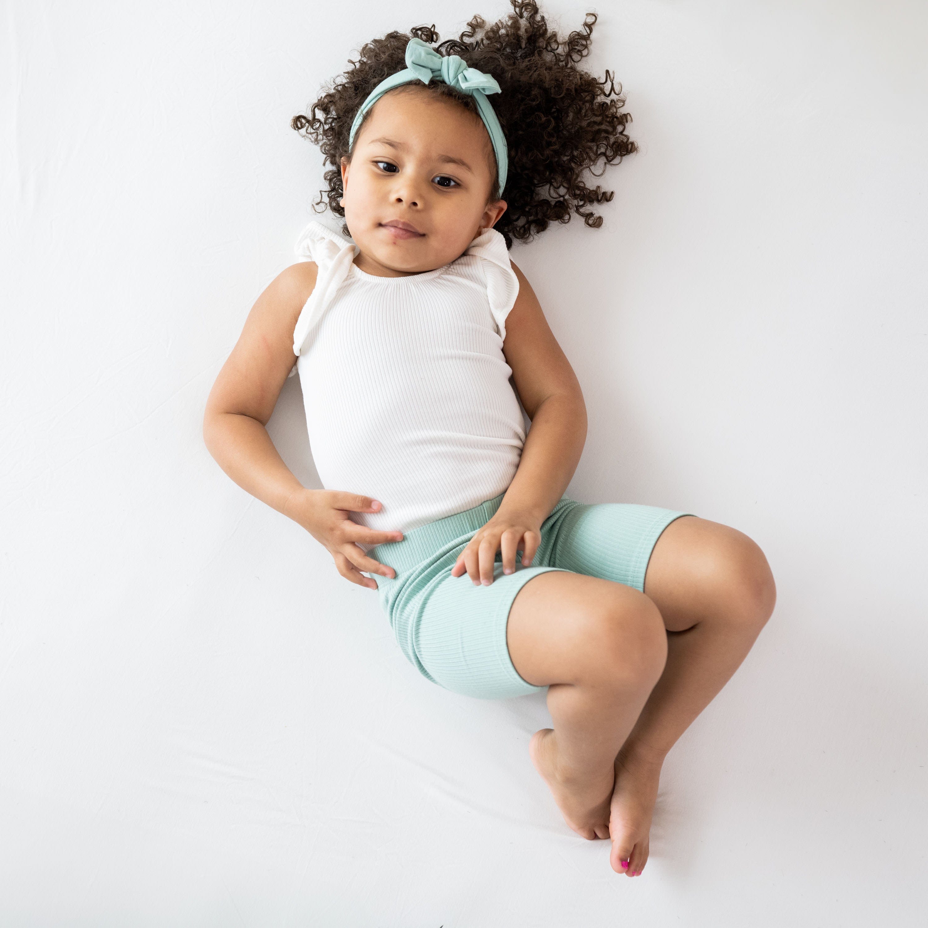 Girl wearing Kyte Baby Ribbed Sleeveless Ruffle Leotard with snap closure in Cloud