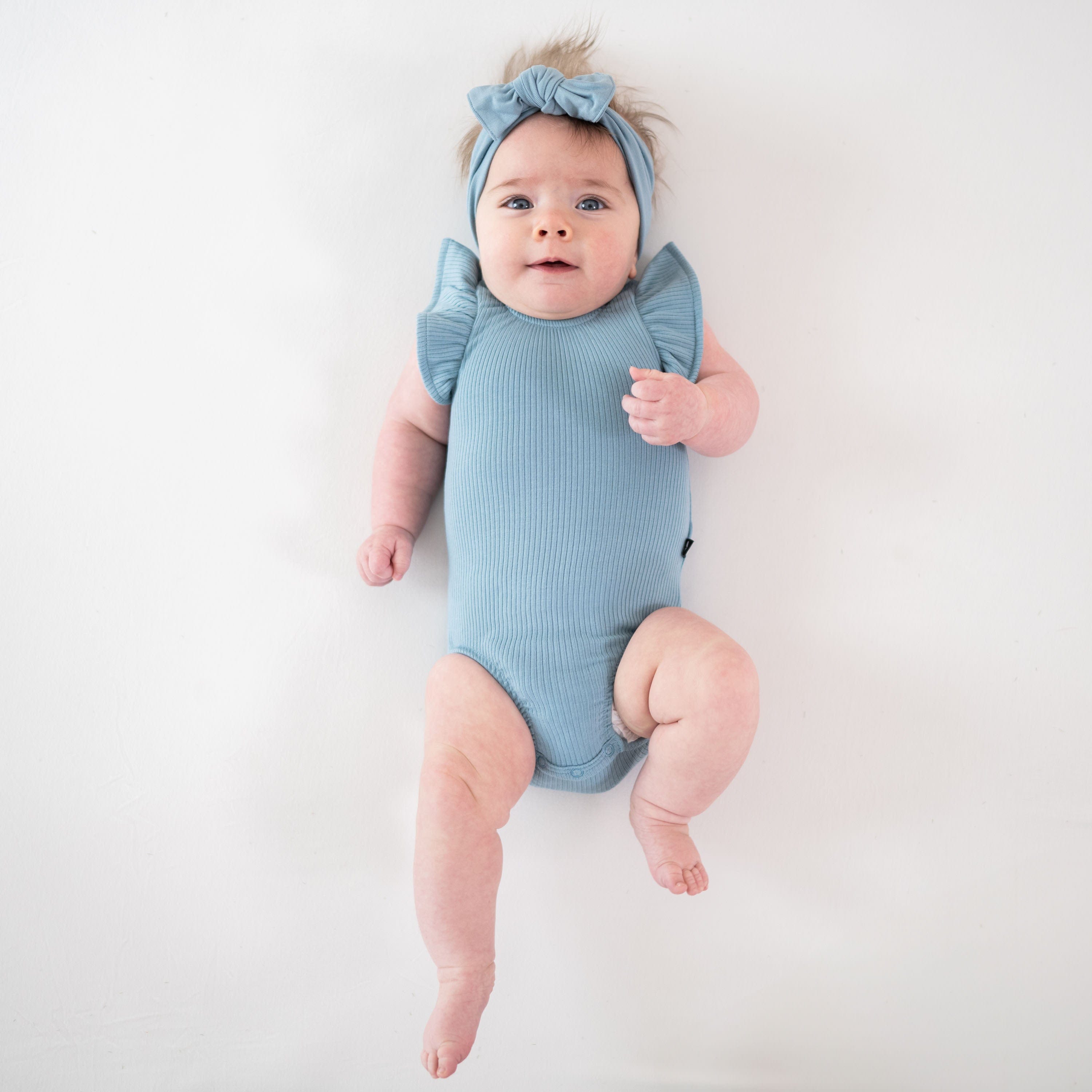 Infant wearing Kyte Baby bamboo Ribbed Sleeveless Ruffle Leotard in Dusty Blue