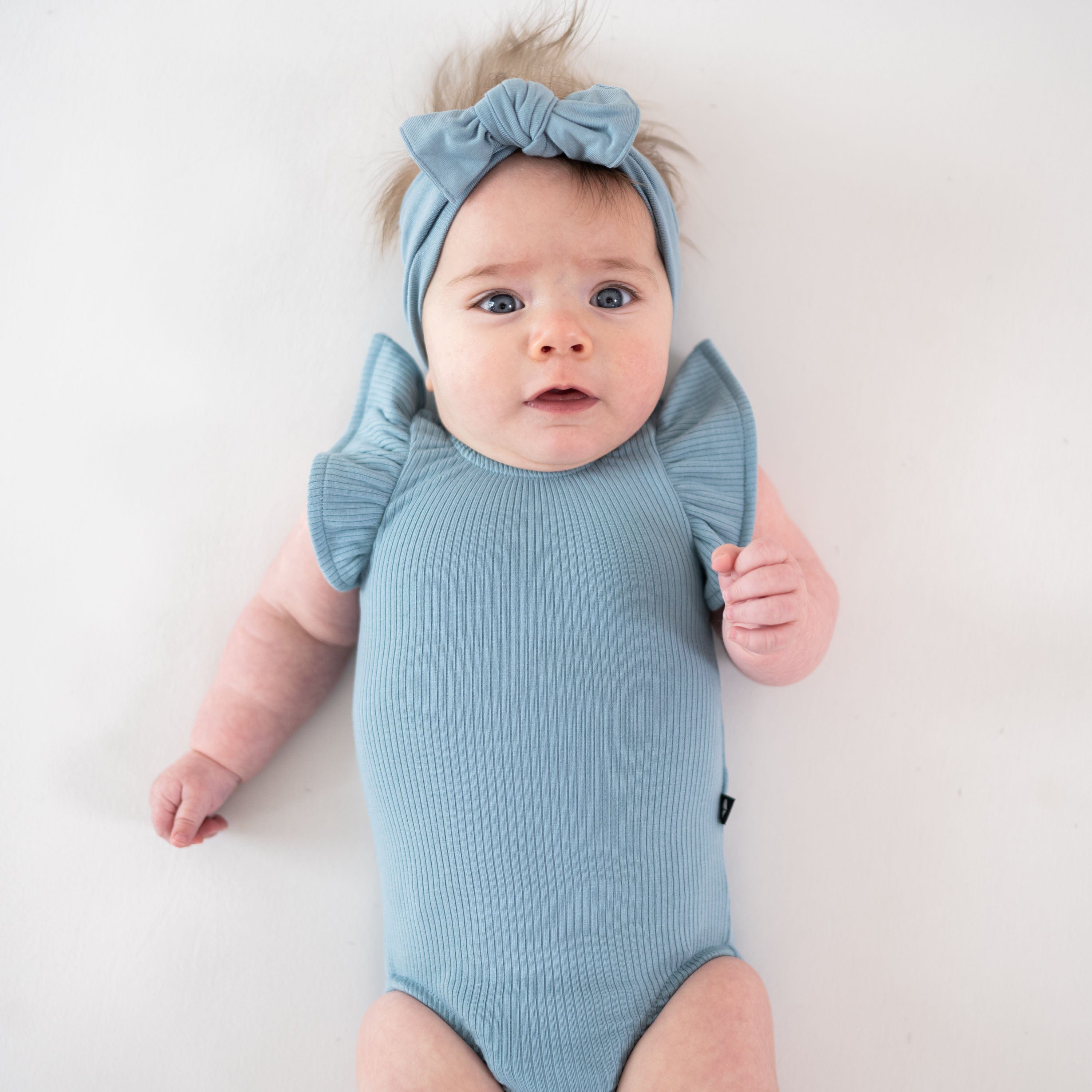 Infant wearing Kyte Baby Ribbed Sleeveless Ruffle Leotard in Dusty Blue