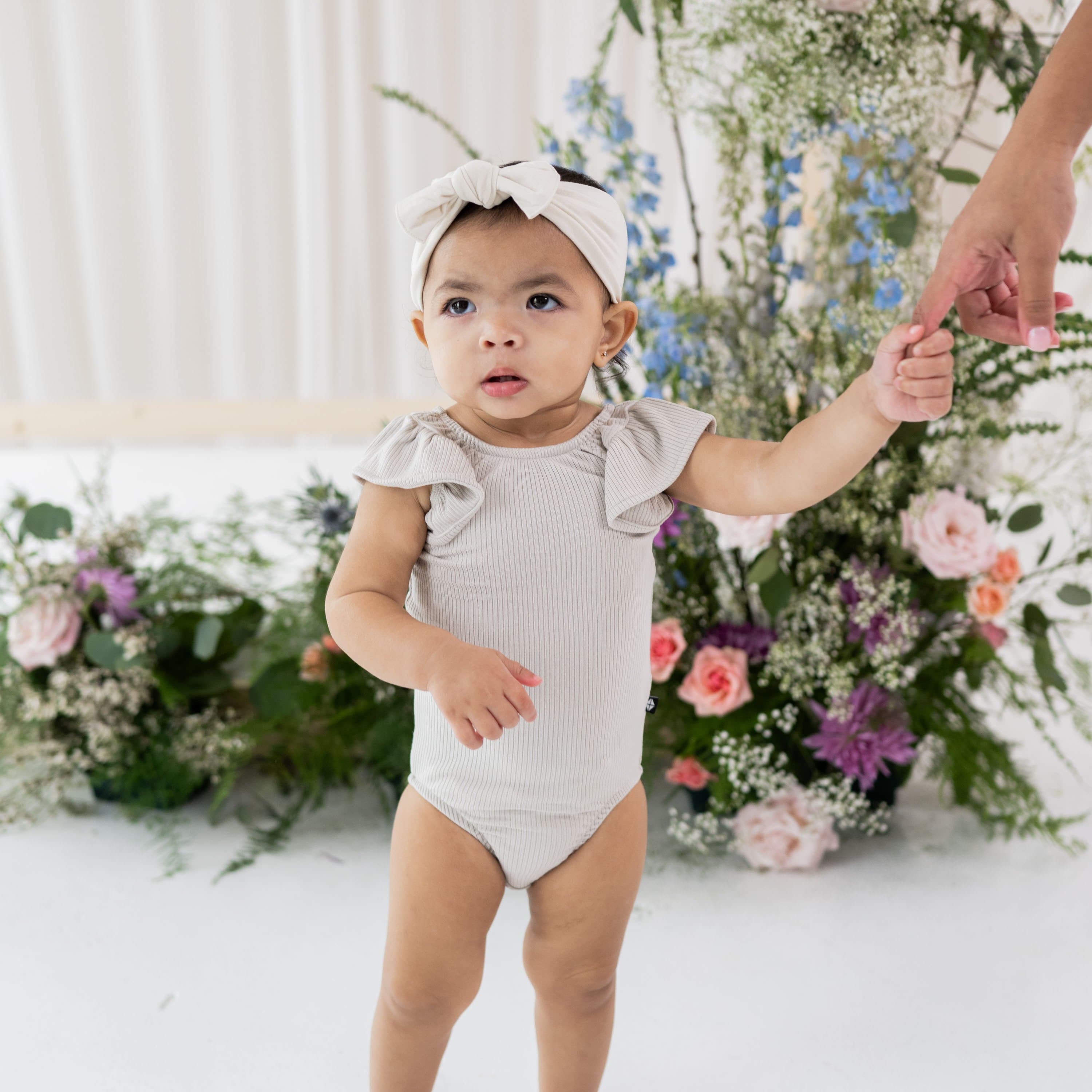 Infant wearing Kyte Baby Ribbed Sleeveless Ruffle Leotard in Oat
