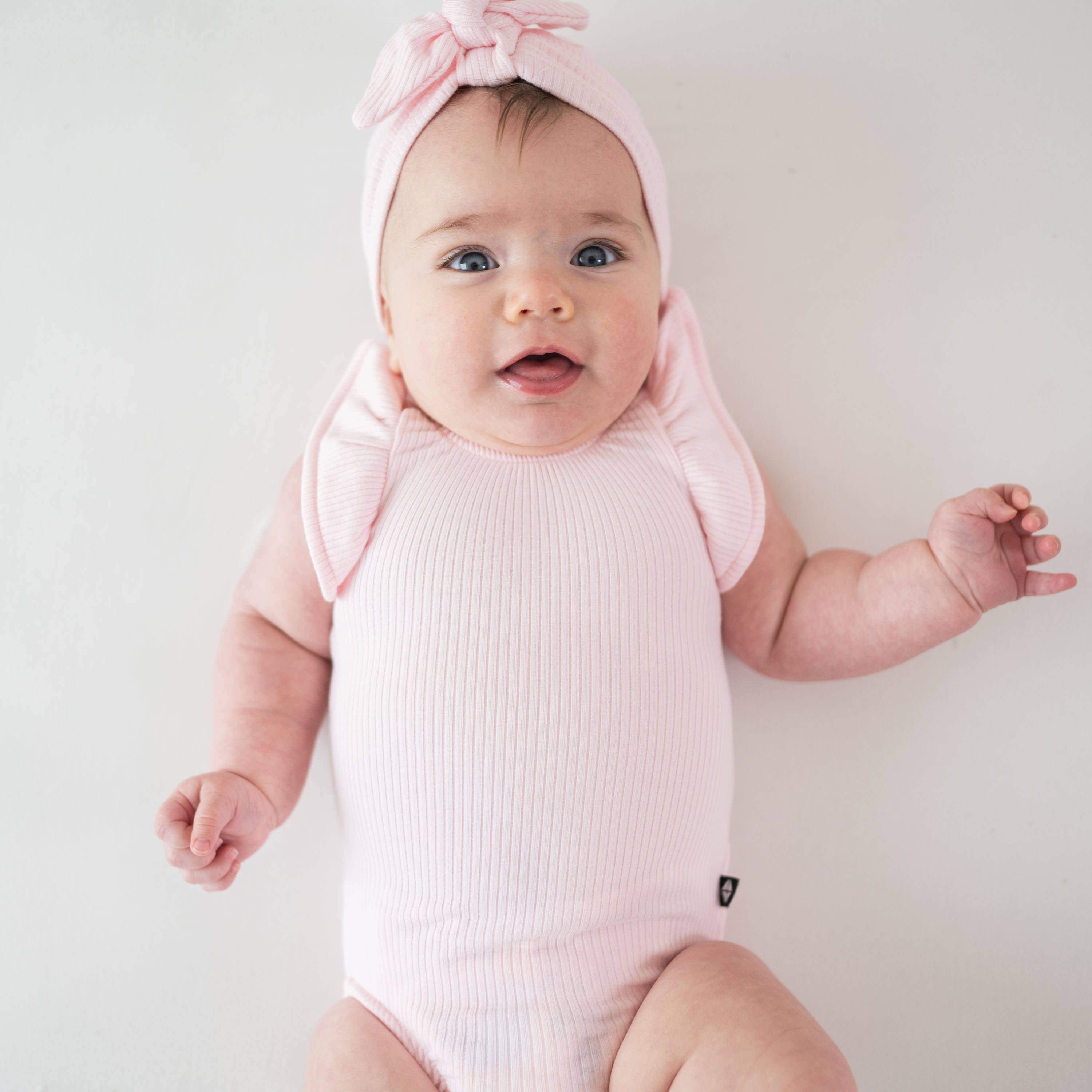 Infant wearing Kyte Baby Ribbed Sleeveless Ruffle Leotard in Sakura