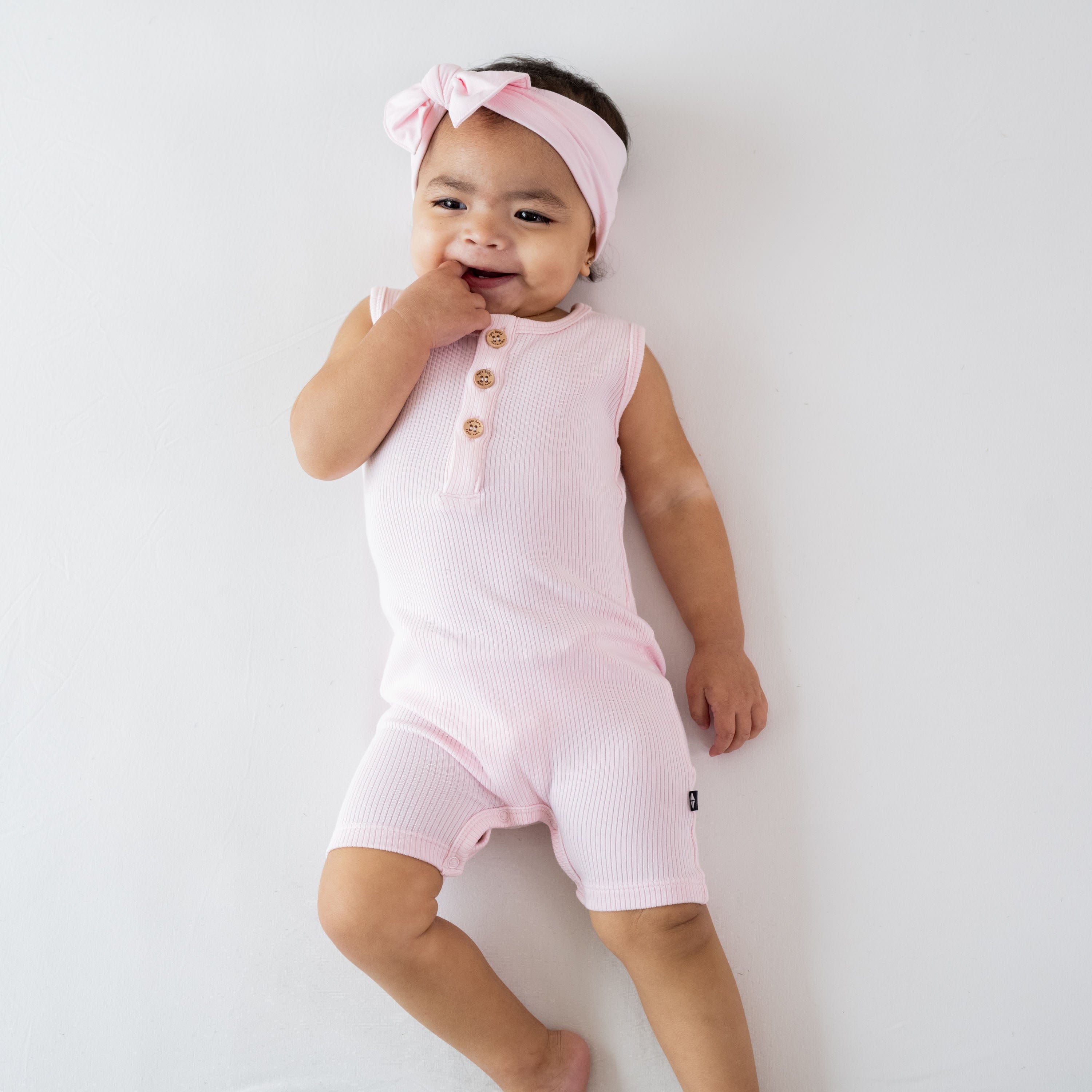 Infant wearing Kyte Baby Ribbed Sleeveless Shortall in Sakura pink