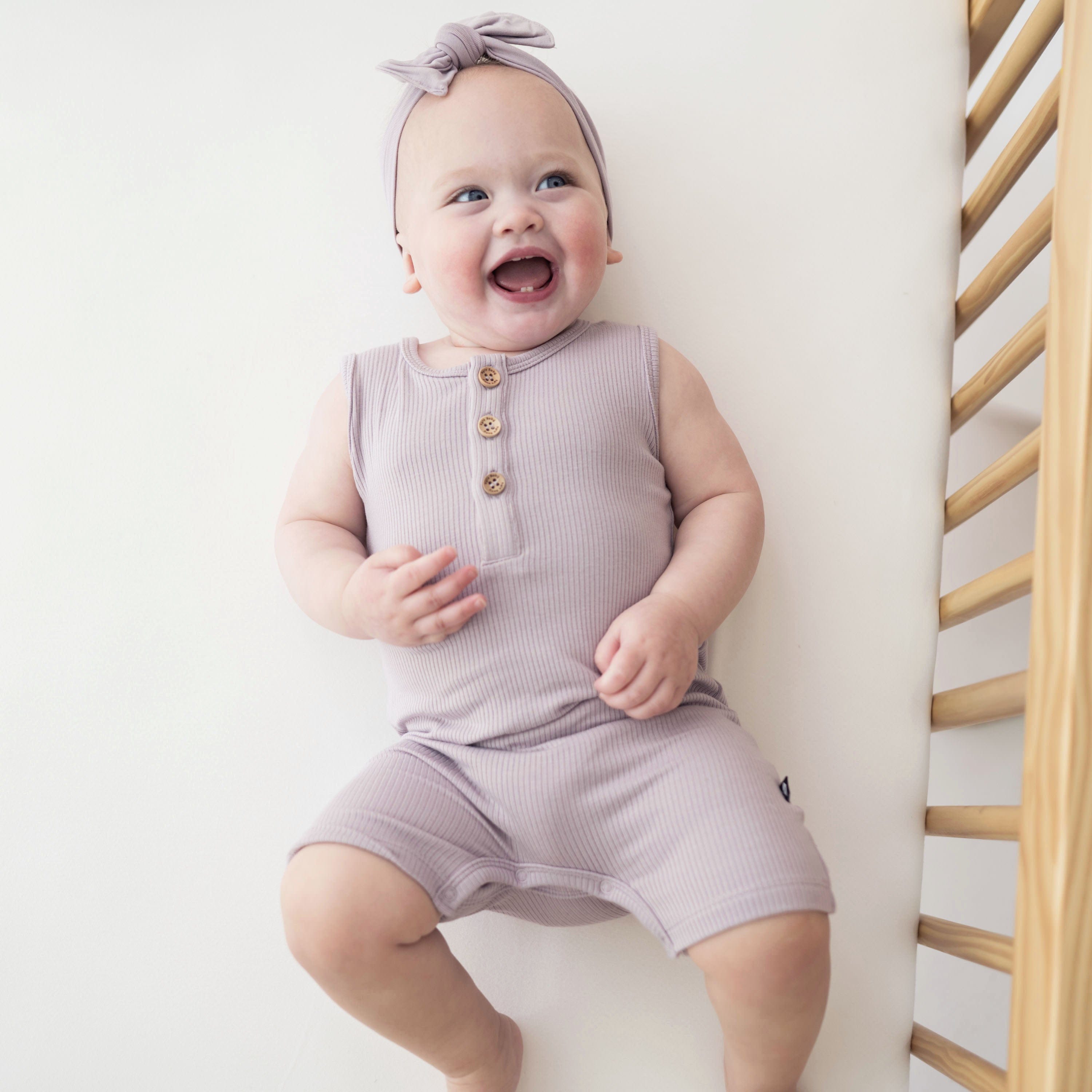 Infant wearing Kyte Baby Ribbed Sleeveless Shortall with henley neckline in Wisteria purple