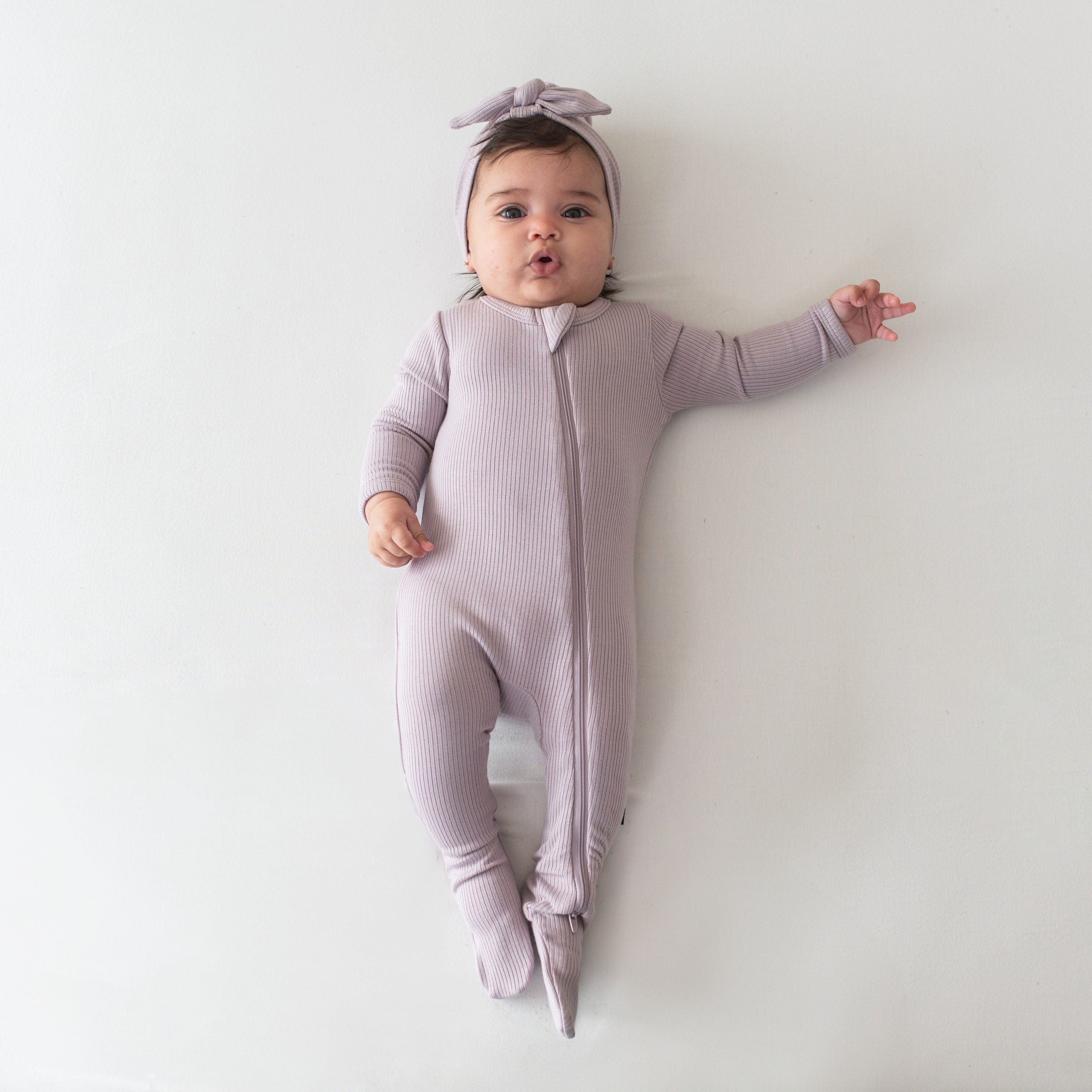 Infant wearing Kyte Baby Ribbed Zipper Footie in Wisteria
