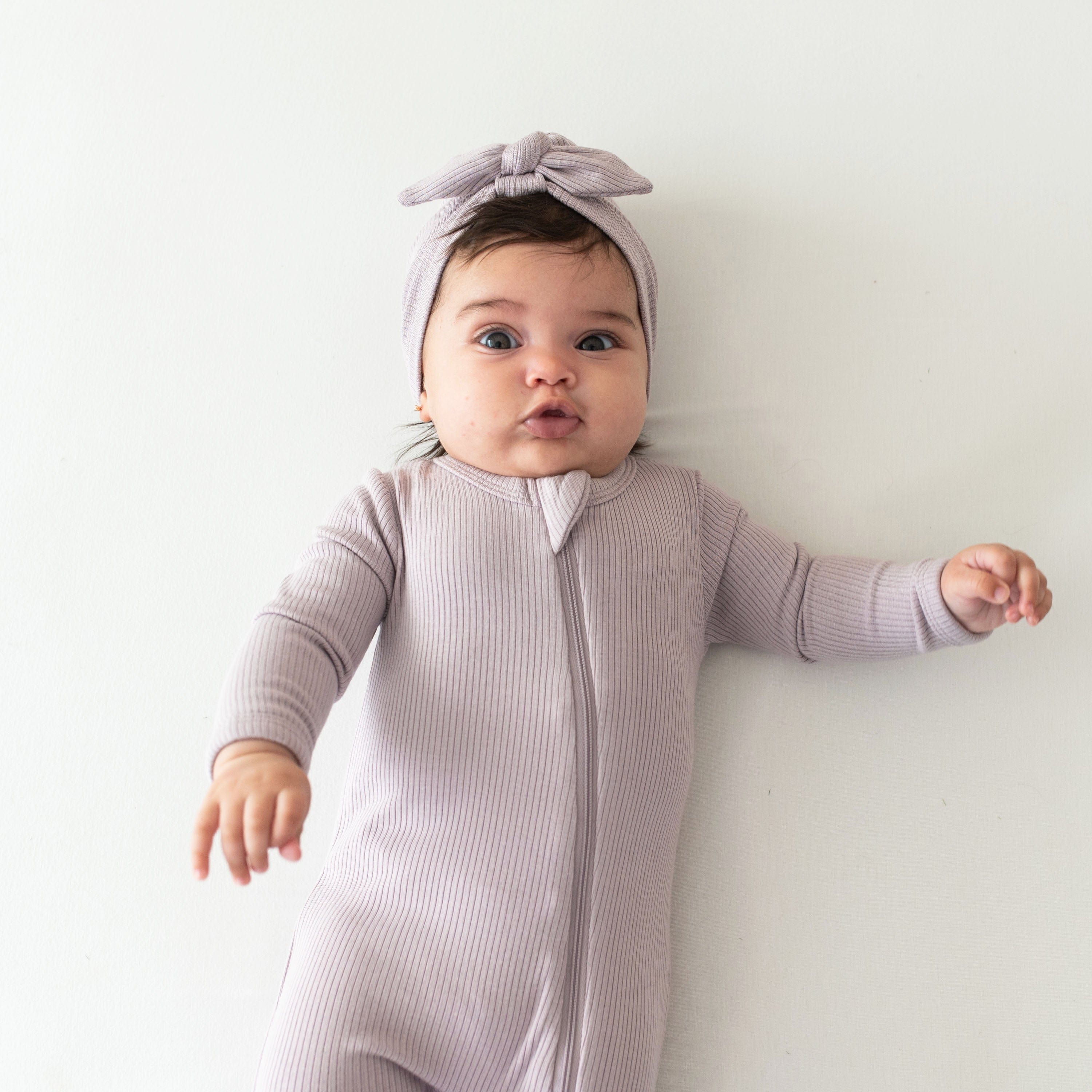 Child wearing Kyte Baby Ribbed Zipper Footie pajamas in Wisteria